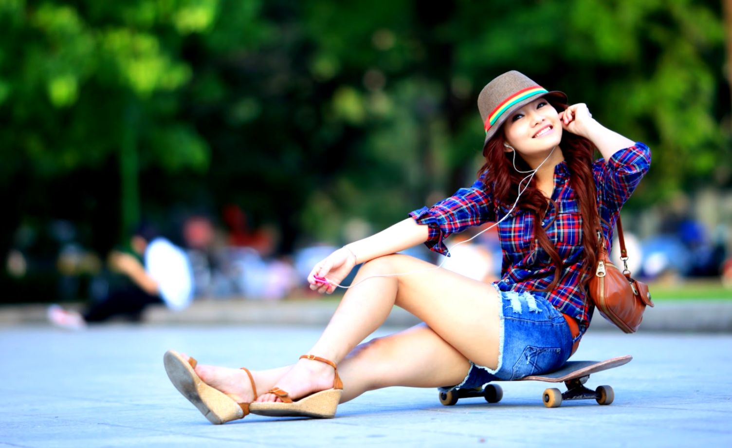 Stylish girl sitting on a skateboard, enjoying music in a park setting