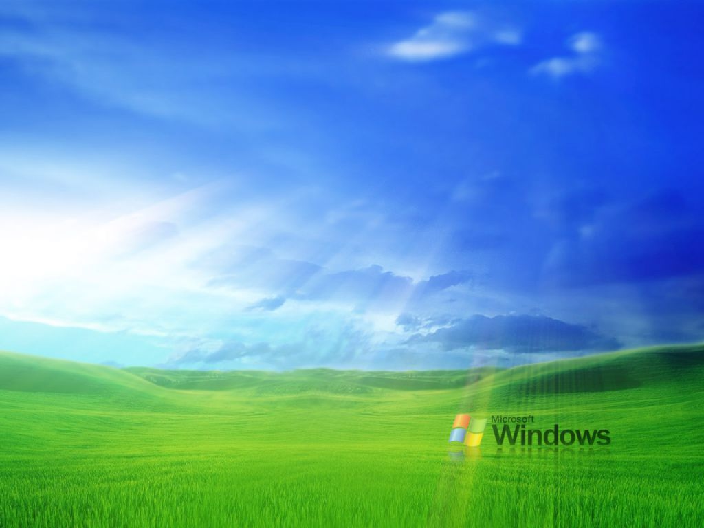 A vibrant green field stretches out under a bright blue sky, reminiscent of the classic Windows Bliss wallpaper. The Microsoft Windows logo is subtly placed in the foreground