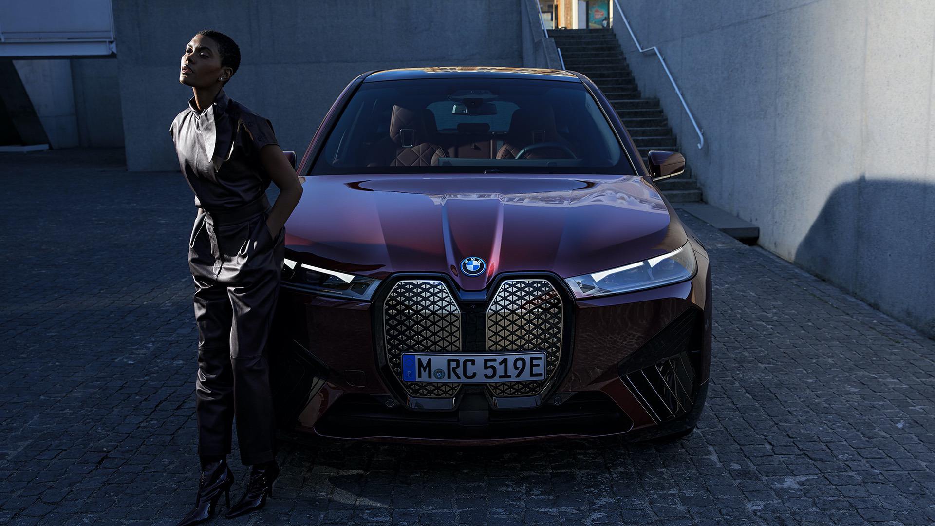 A stylish woman stands next to a maroon BMW iX electric SUV, highlighting its sleek design and luxurious appeal