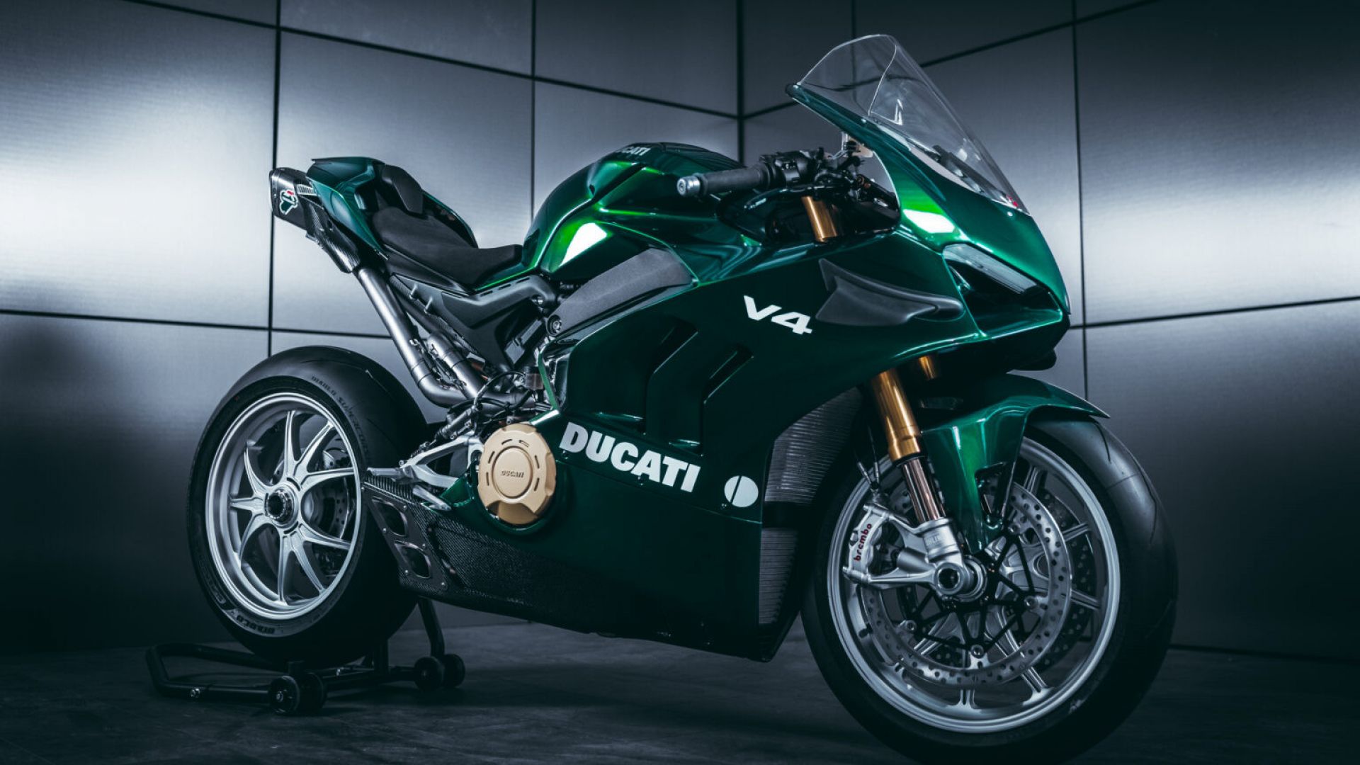 A Ducati V4 motorcycle, finished in a deep green, sits on display in a modern, minimalist setting. The bike's sleek design and high-performance features are evident in its aggressive stance and premium components
