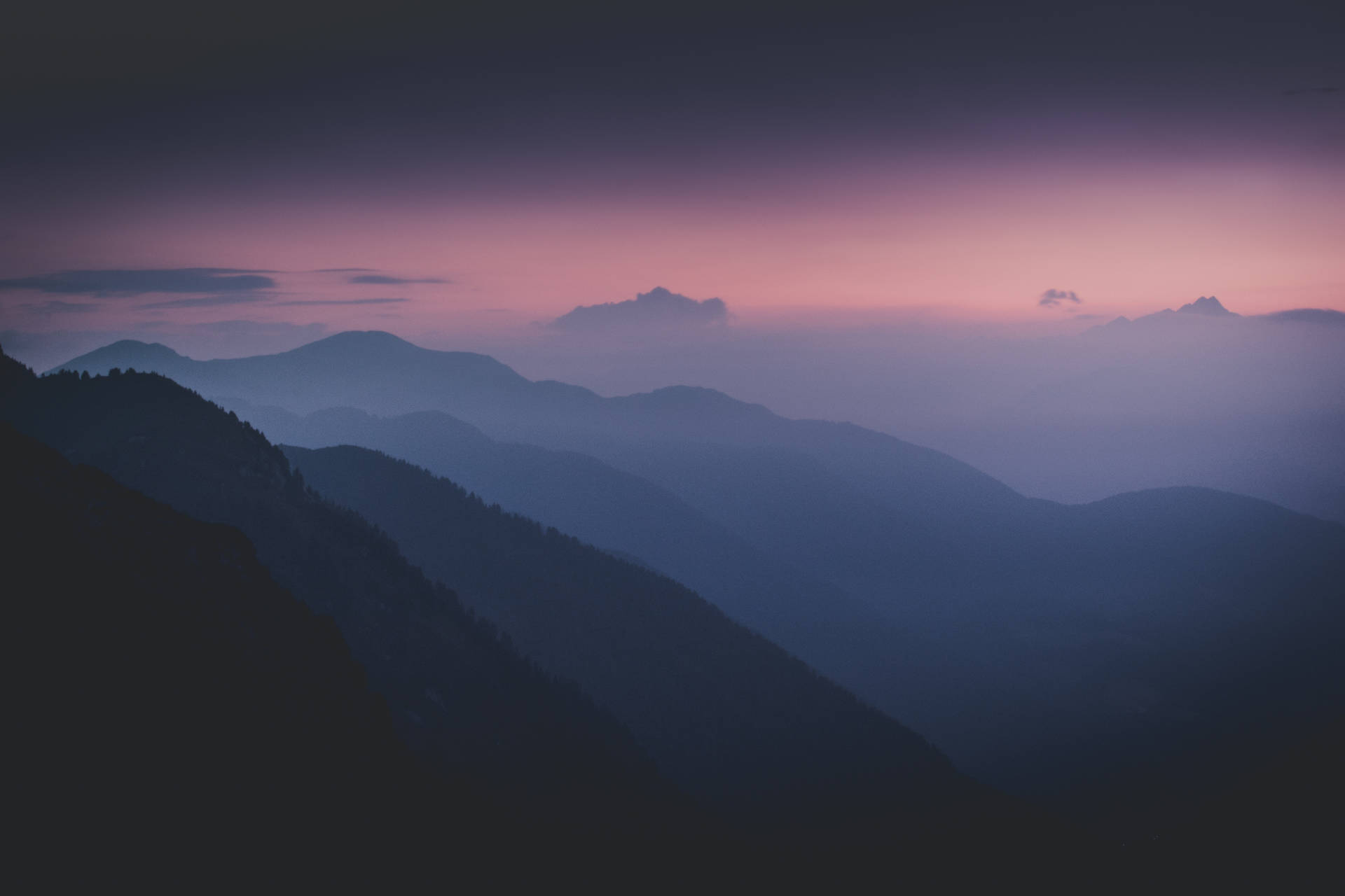 Silhouetted mountain ranges fade into a hazy, pastel sunset sky