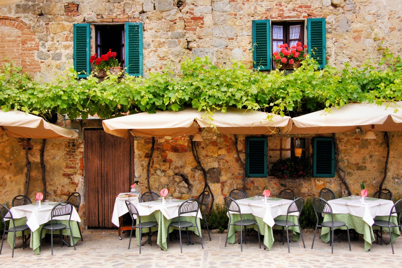 Cafe Tables And Chairs Outside A Quaint Stone Building In Tuscany