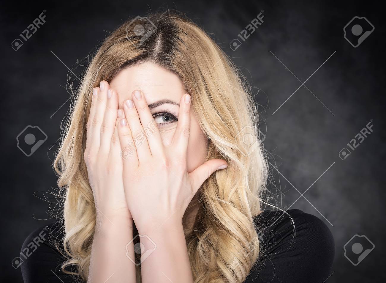 Woman Peeping Through Her Fingers Over Dark Background Stock Photo