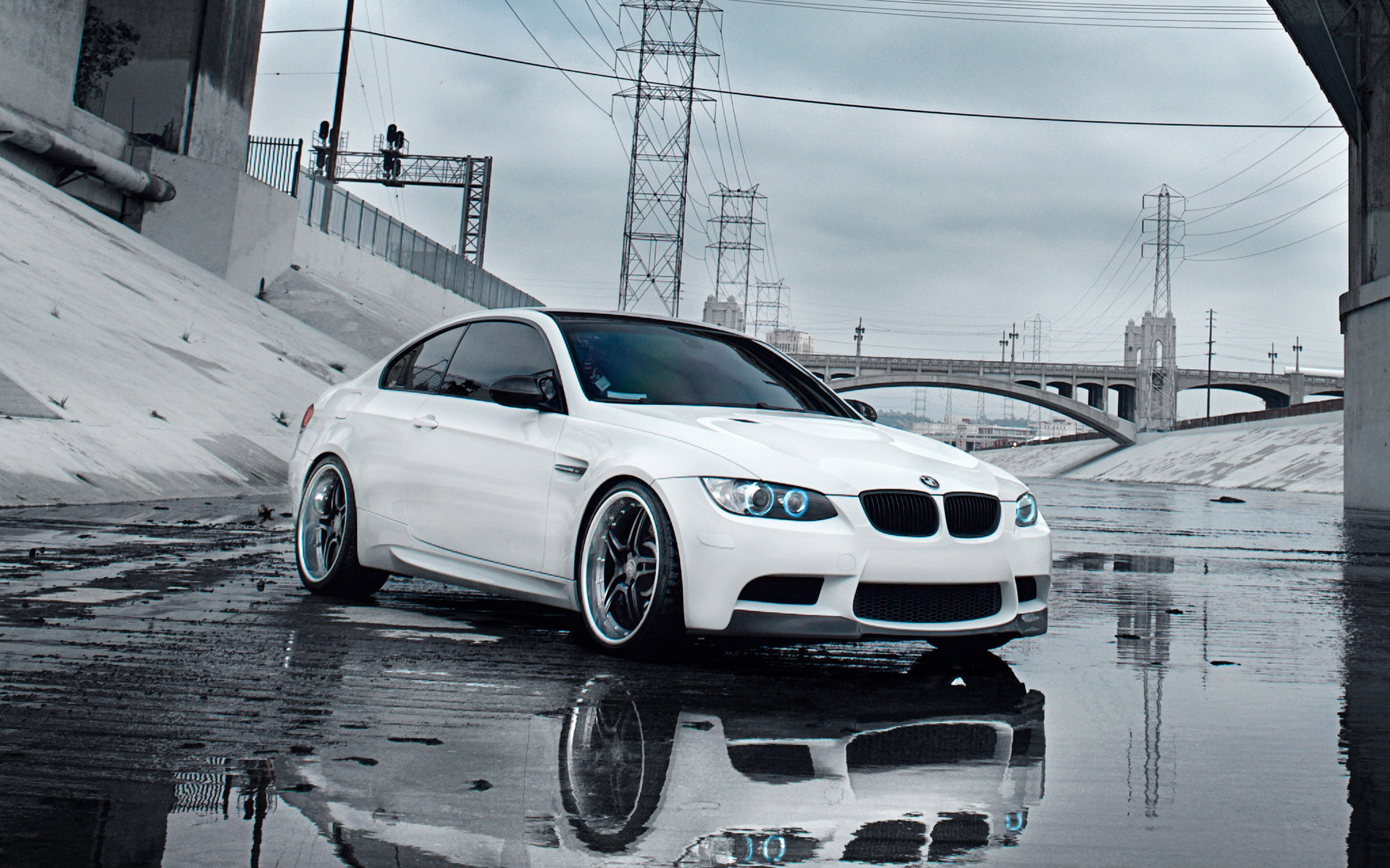White BMW M3 parked under a bridge in a wet cityscape