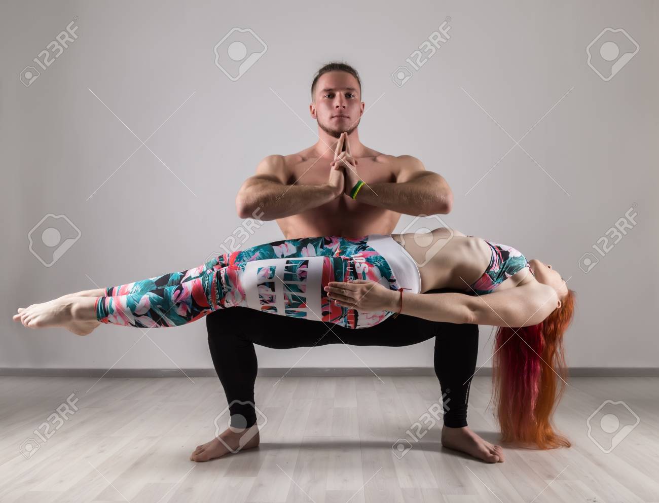 Sports Man And Woman Doing Acroyoga Exercises In A Gray Background