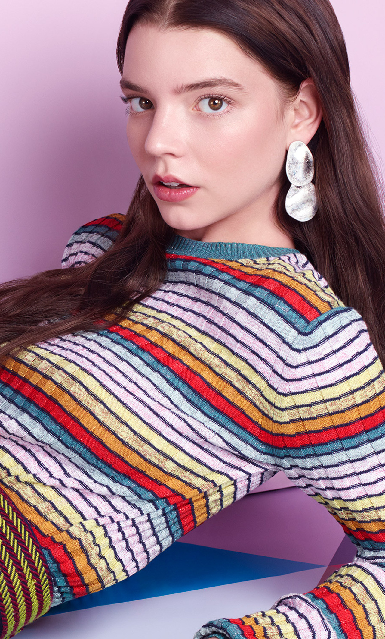Anya Taylor-Joy in a colorful striped sweater, posing against a vibrant backdrop