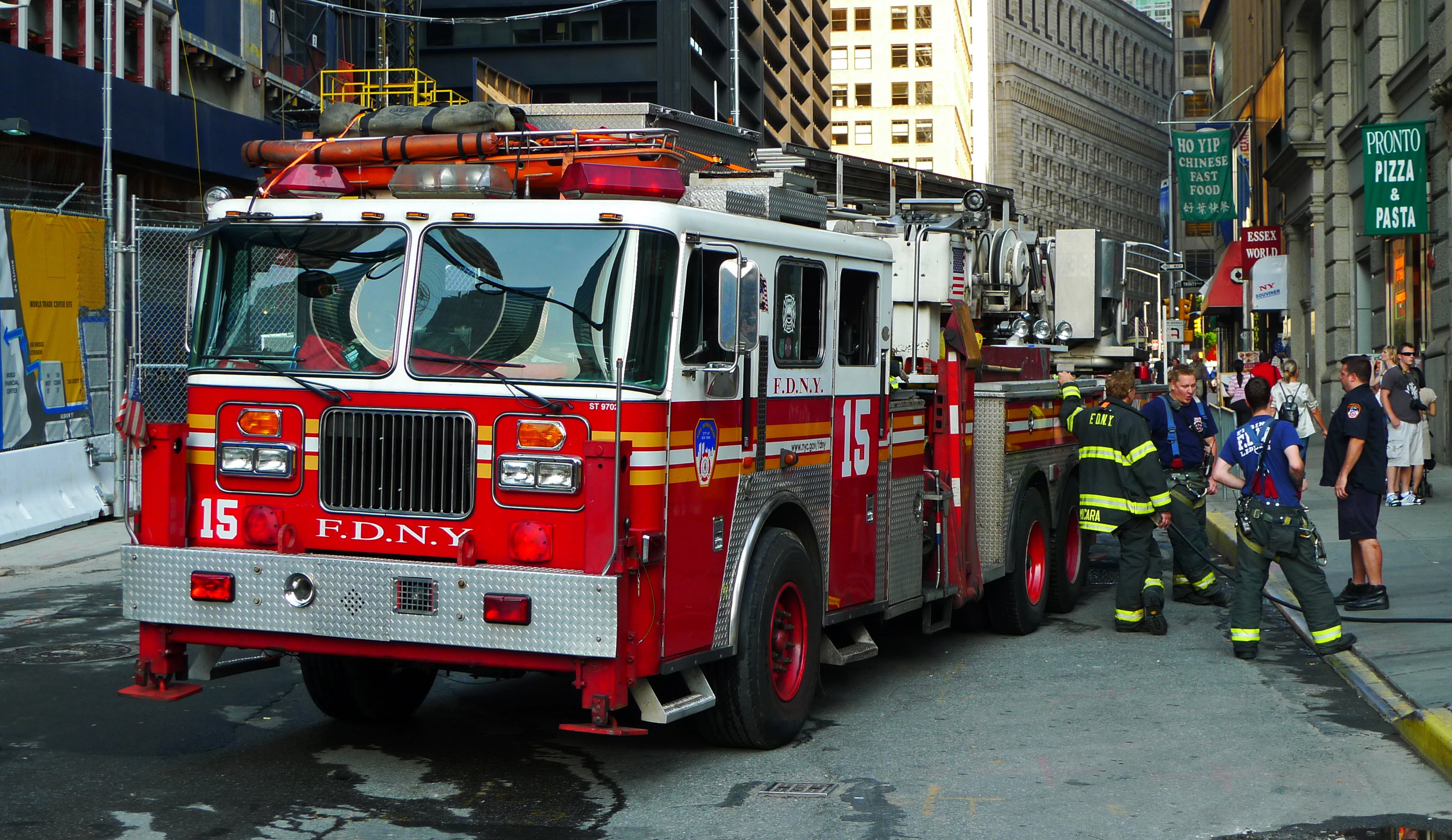 A New York City Fire Department (FDNY) fire engine parked on a city street, with firefighters preparing for action