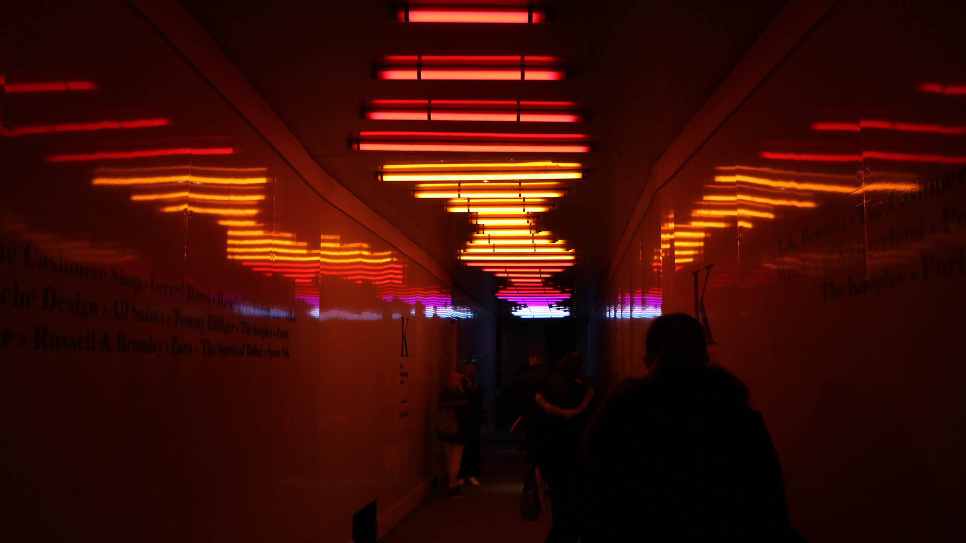 A dimly lit hallway with vibrant neon lights reflecting on the walls, creating an abstract and futuristic atmosphere