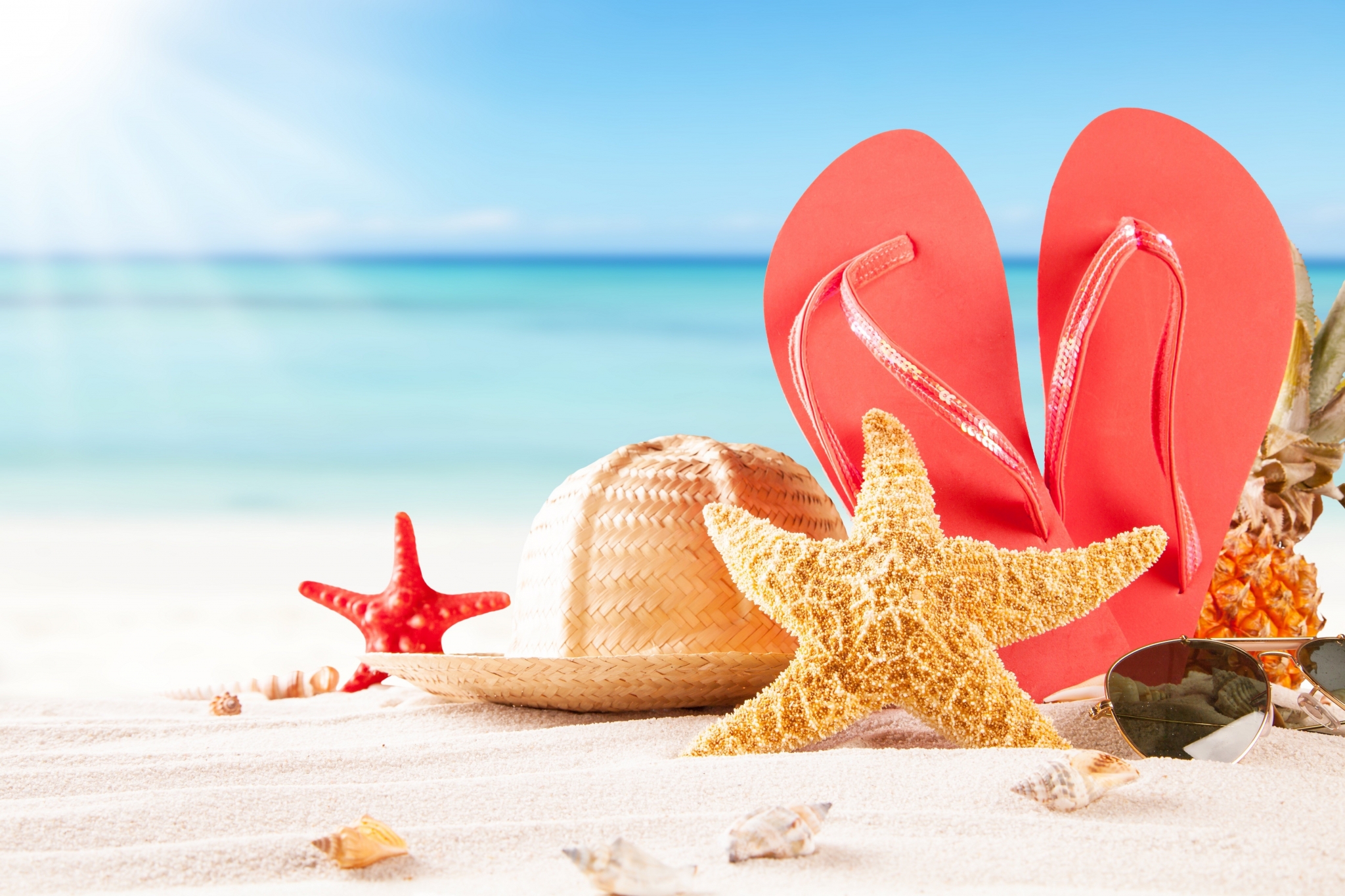 Summer beach scene with flip-flops, hat, starfish, and pineapple on white sand