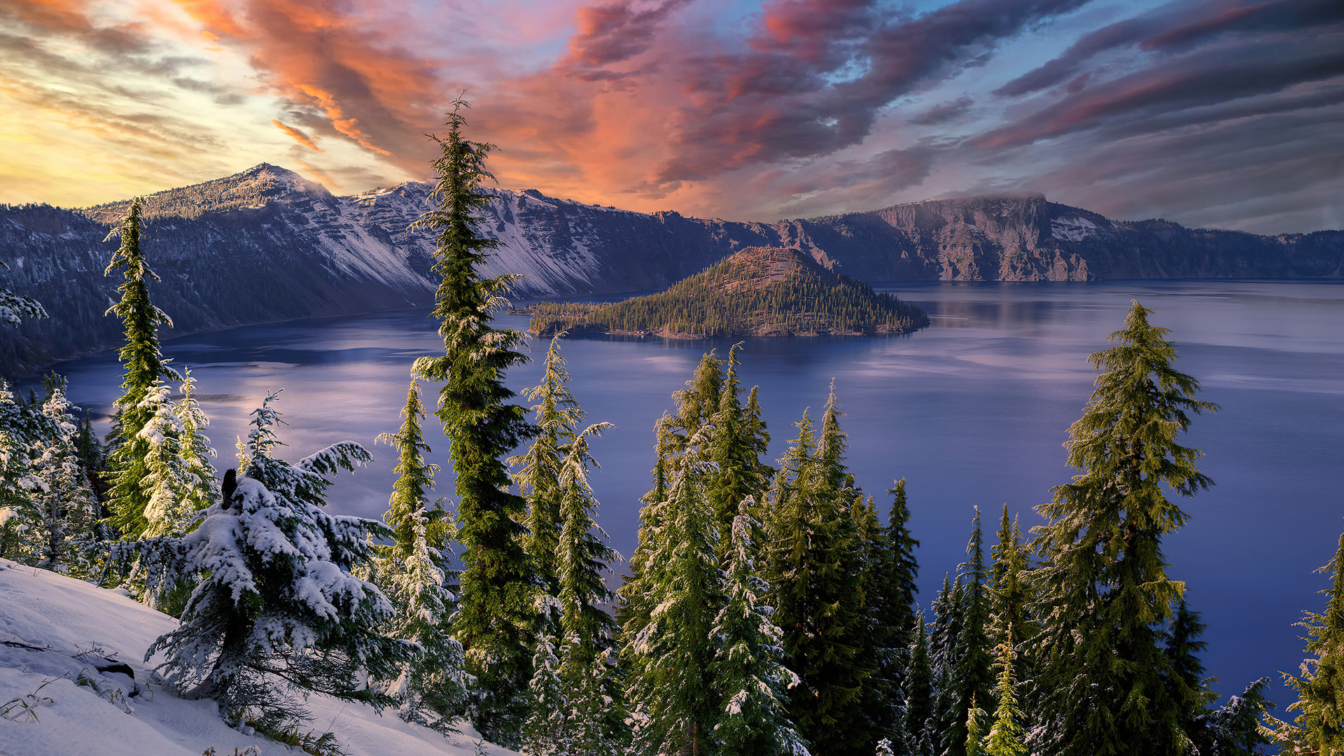 A breathtaking winter sunrise over Crater Lake National Park, with snow-dusted pine trees in the foreground and Wizard Island in the distance