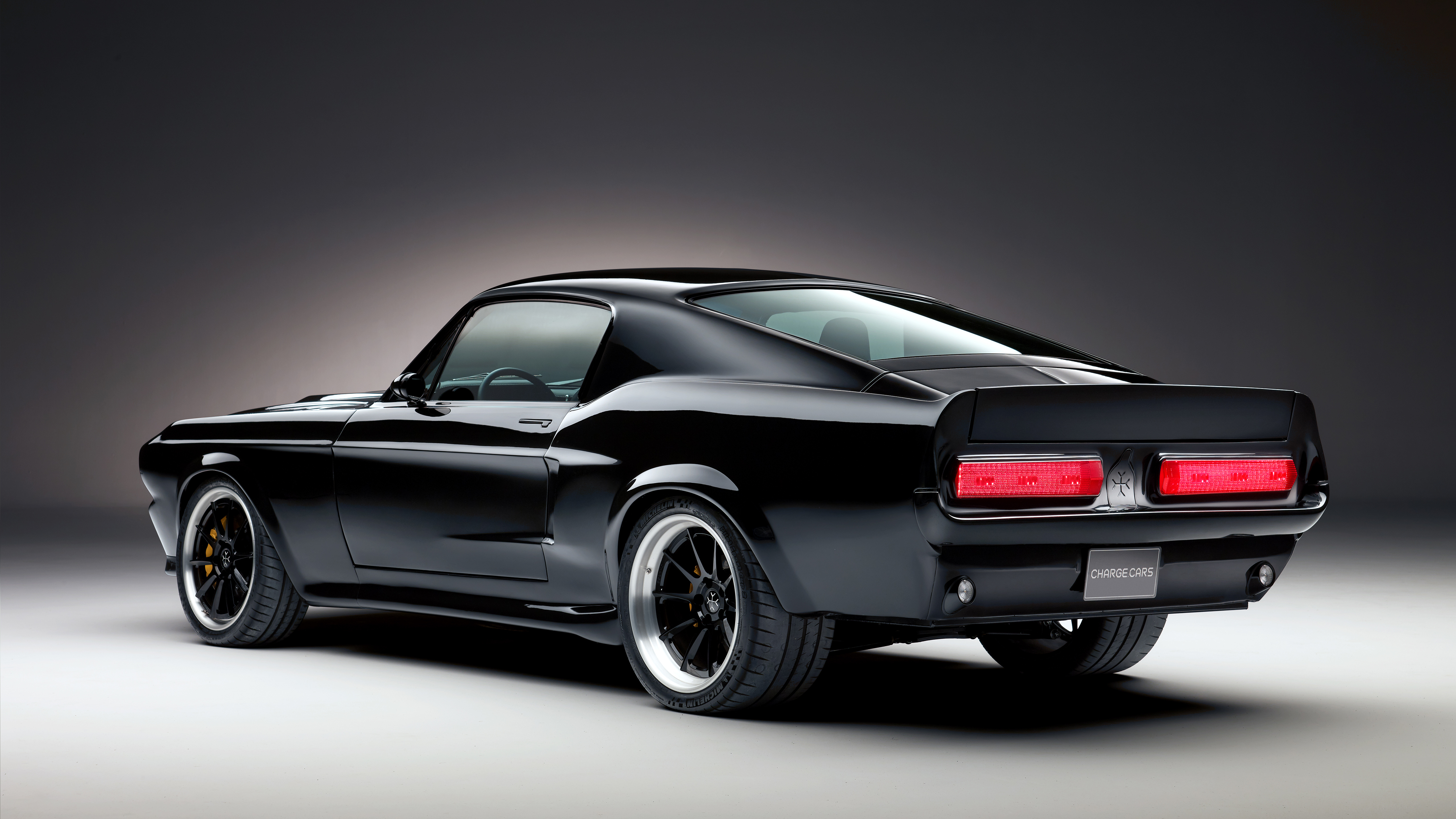 A sleek, black classic Ford Mustang, possibly a modified Shelby GT500, is showcased against a dark studio backdrop. The car's glossy finish reflects the minimal lighting, highlighting its powerful stance and iconic design