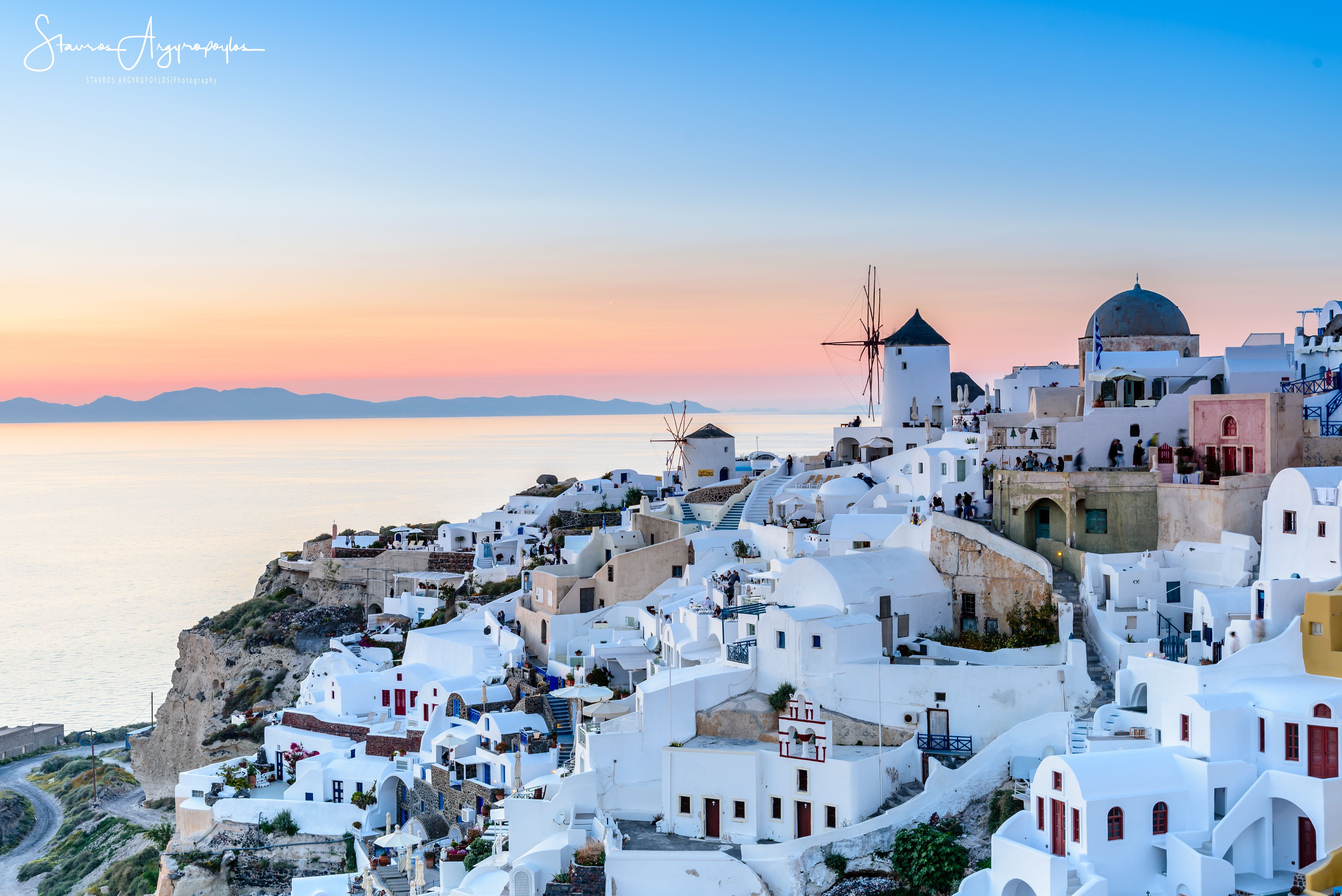 White-walled buildings perched on a cliff overlooking the Aegean Sea at sunset, Santorini, Greece