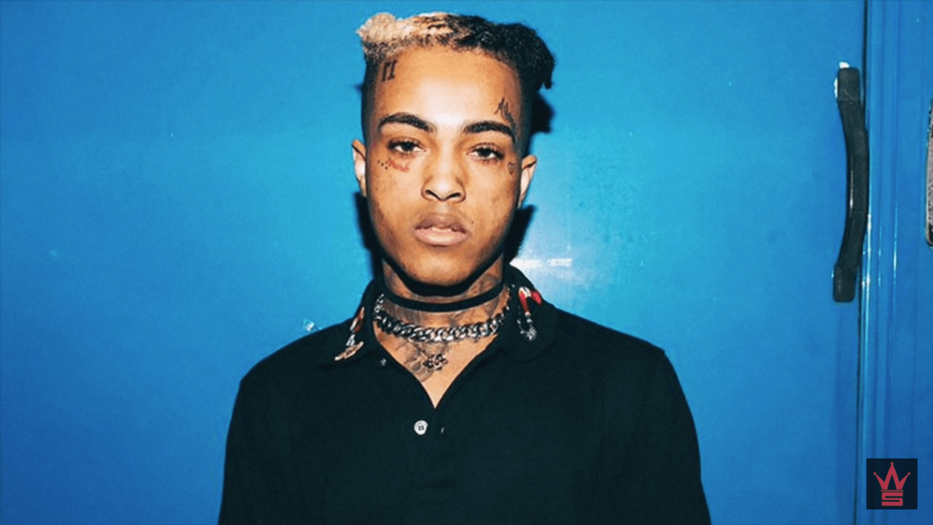 Close-up of XXXTentacion against a blue background, showcasing his unique hairstyle and facial tattoos