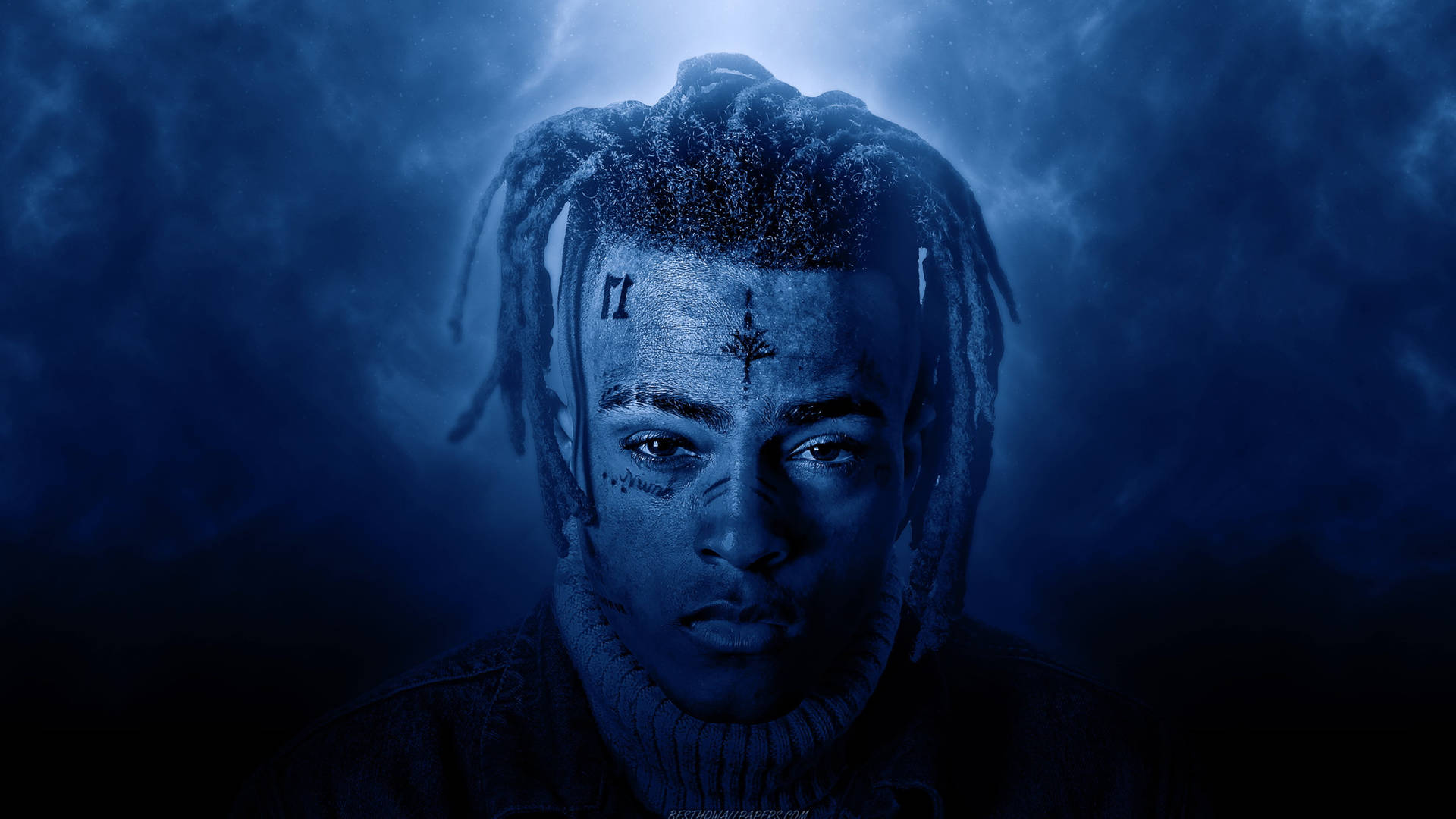 A moody, blue-toned close-up portrait of XXXTentacion, highlighting his distinctive facial tattoos and dreadlocks against a dramatic, cloudy backdrop
