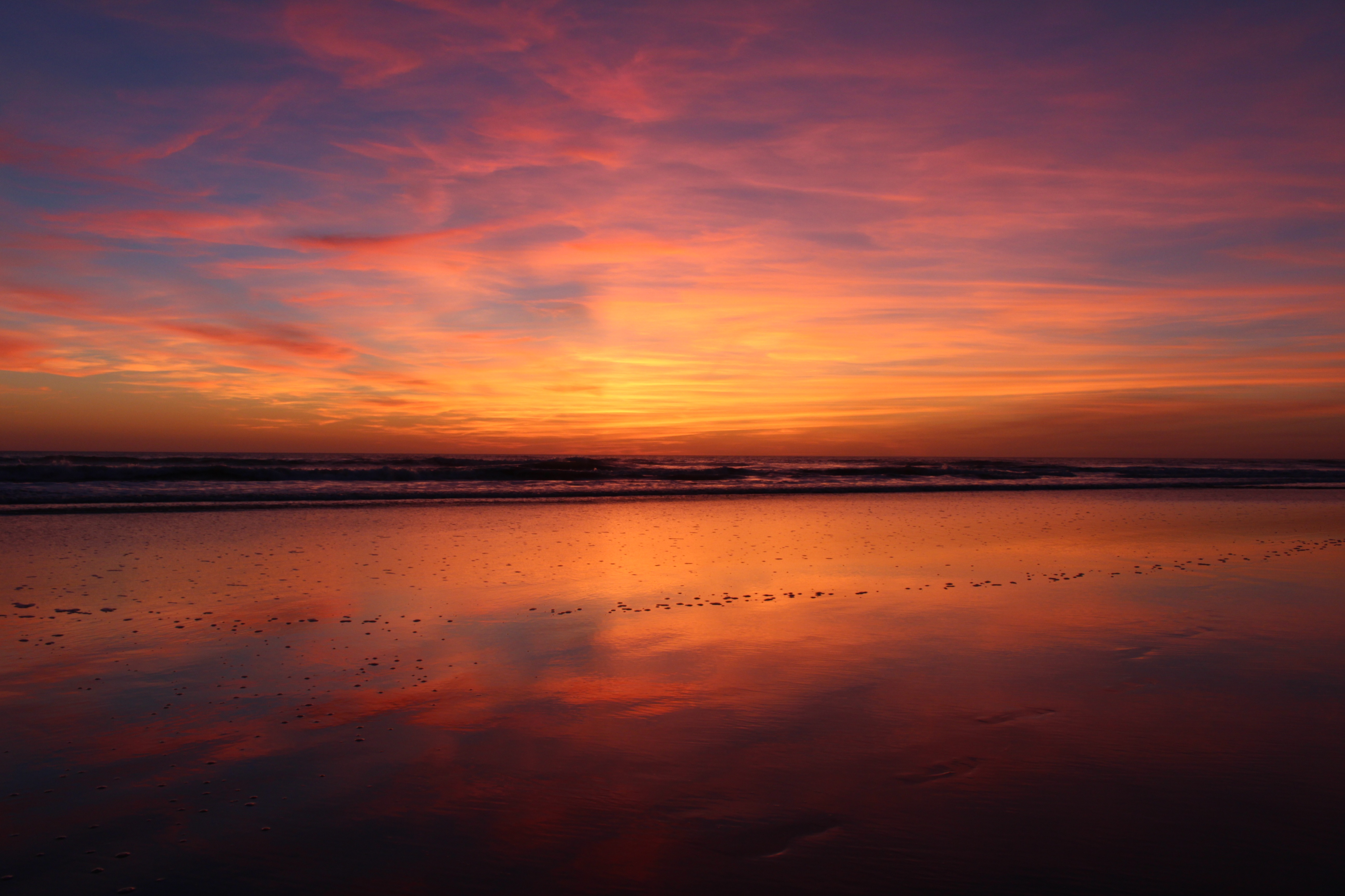 Vivid sunset over a calm beach reflecting the colorful sky, with gentle waves lapping at the shore