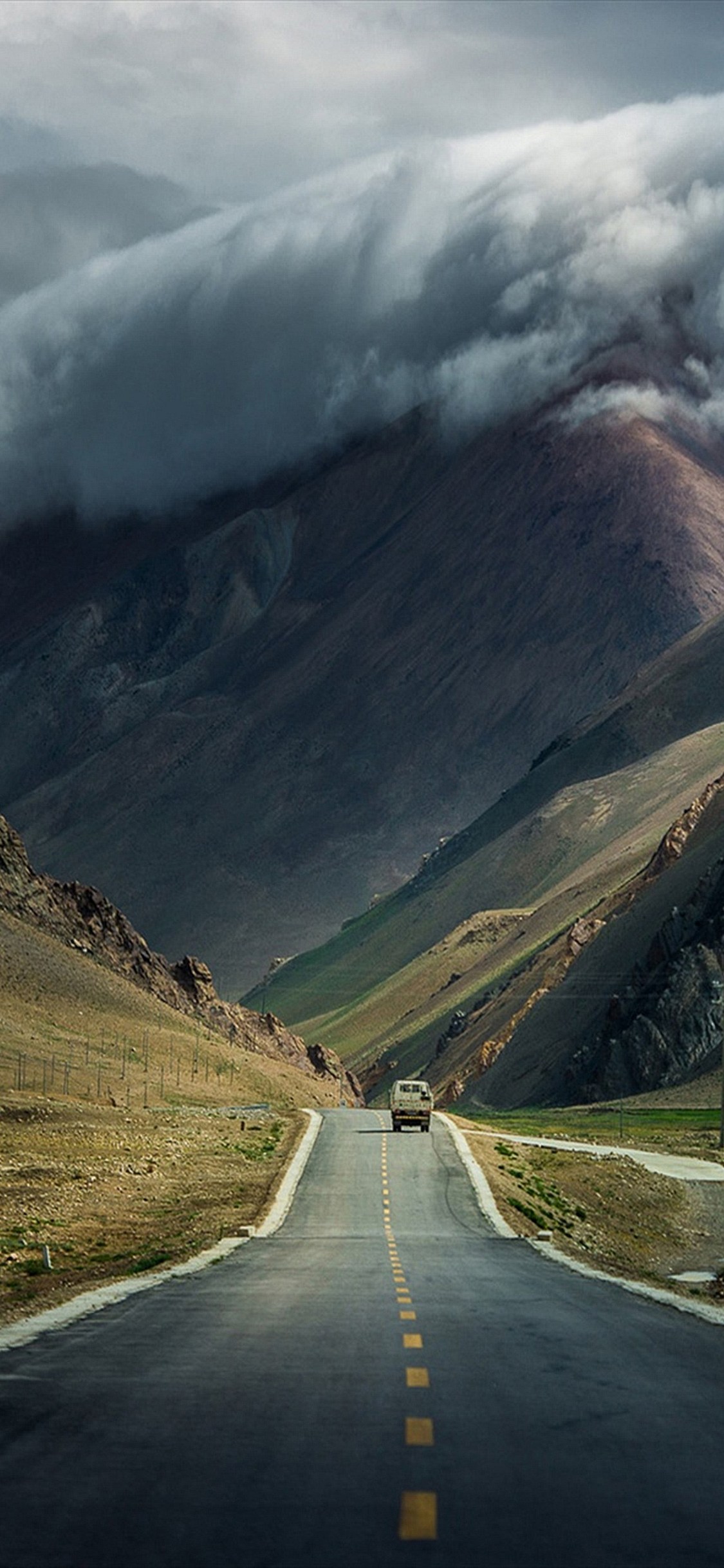 A winding mountain road under a dramatic cloudscape in the Himalayas, possibly taken with an iPhone 14 Pro Max