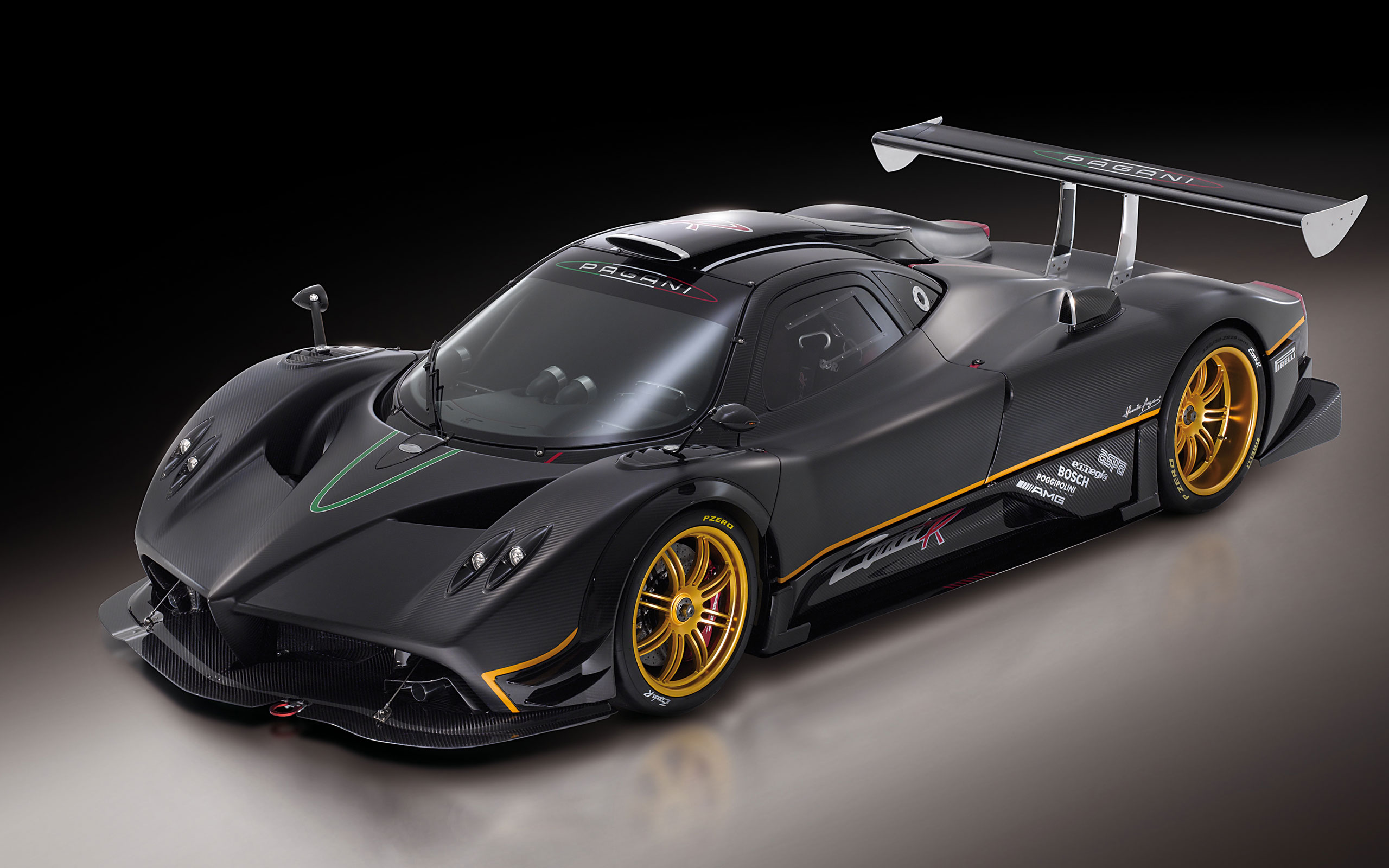 A sleek, black Pagani Zonda R supercar with gold rims and a large rear wing, shown against a dark background