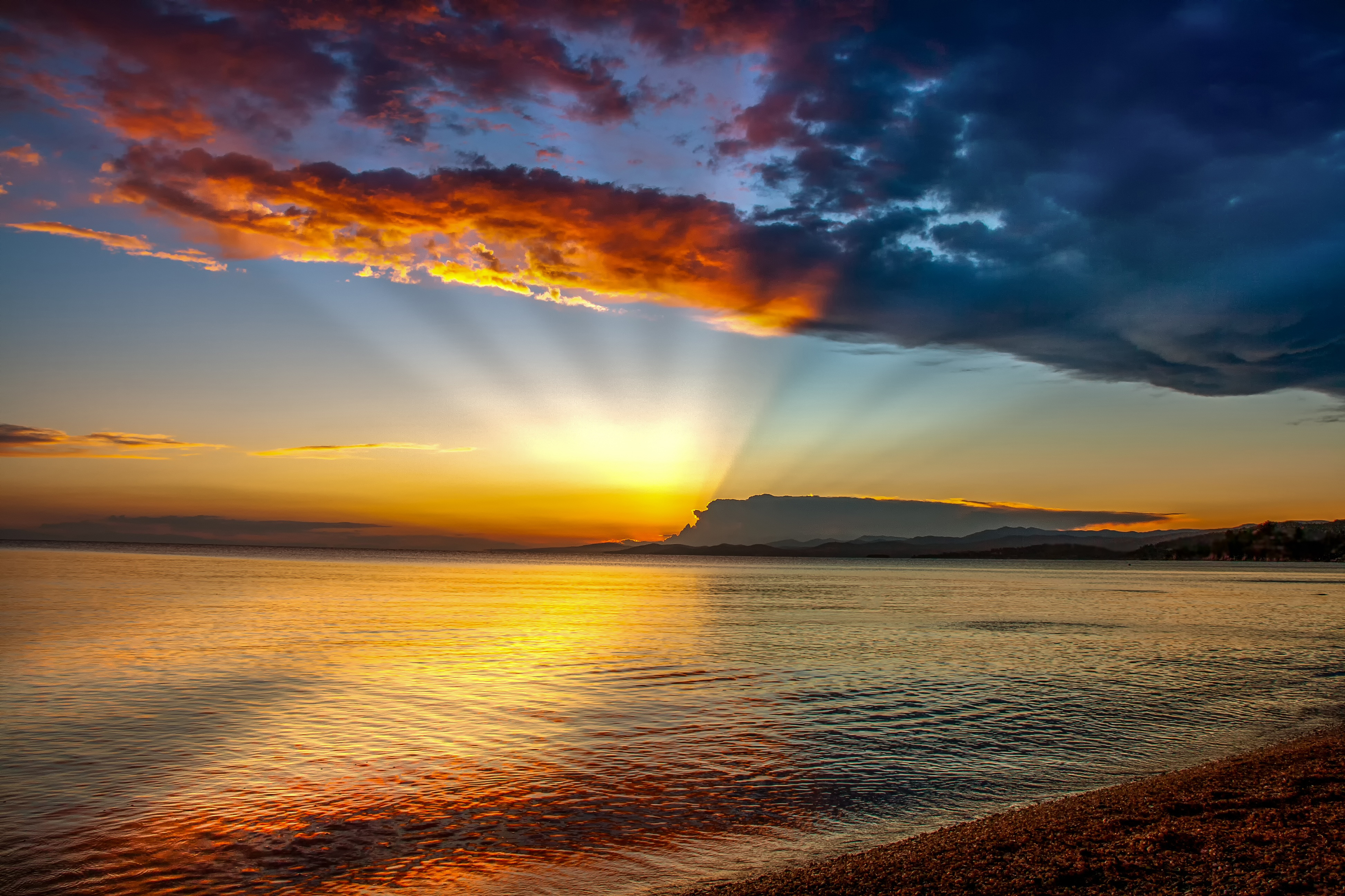 A breathtaking sunset over a tranquil sea, with vibrant orange and red hues reflecting on the water's surface, and crepuscular rays peeking through the clouds