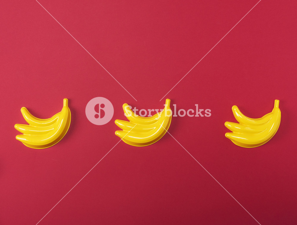 yellow plastic baby toy banana on a red background copy space