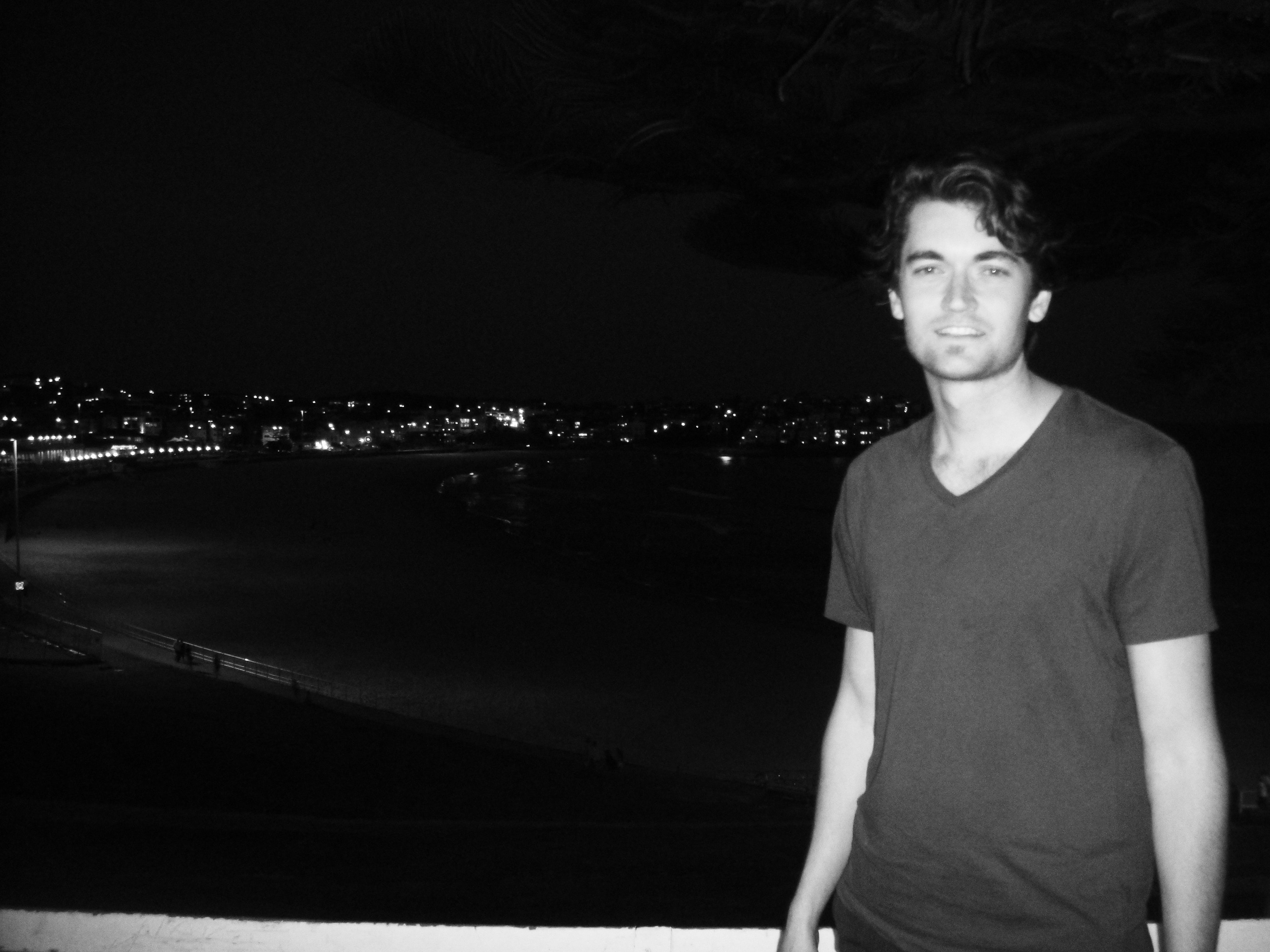 A black and white photo of a young man standing in front of a night view of a cityscape