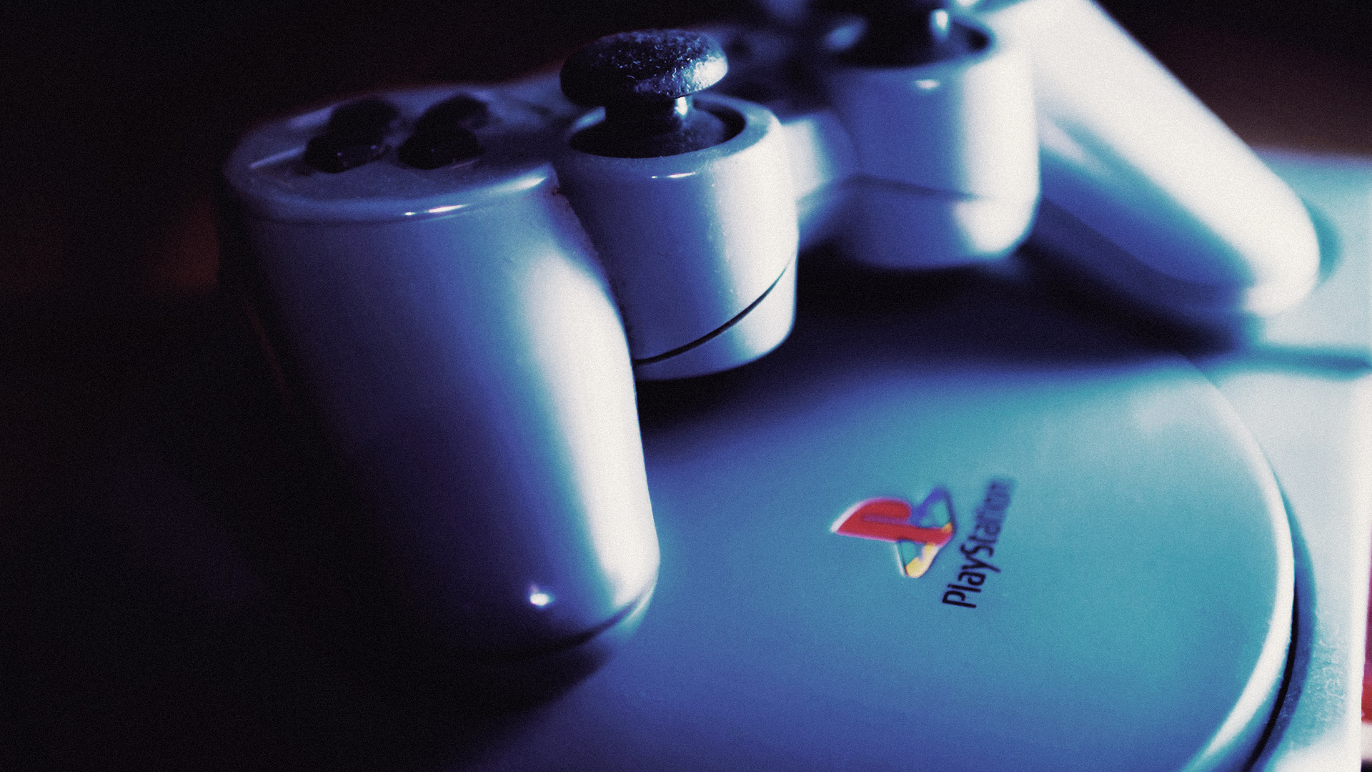 Close-up of a PlayStation controller resting on a PlayStation console, highlighting the iconic logo and buttons