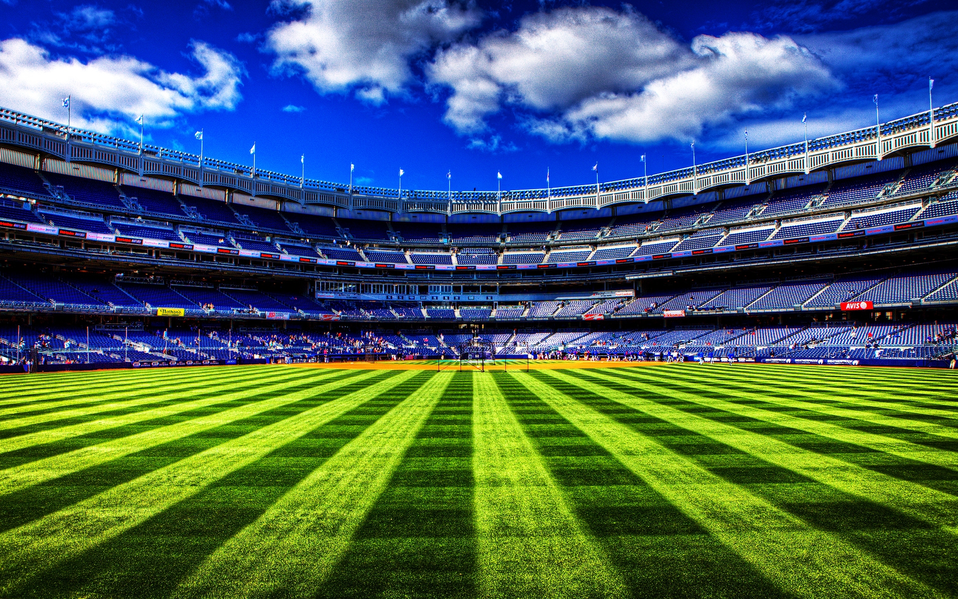 A vibrant green baseball field with a stadium in the background under a bright blue sky