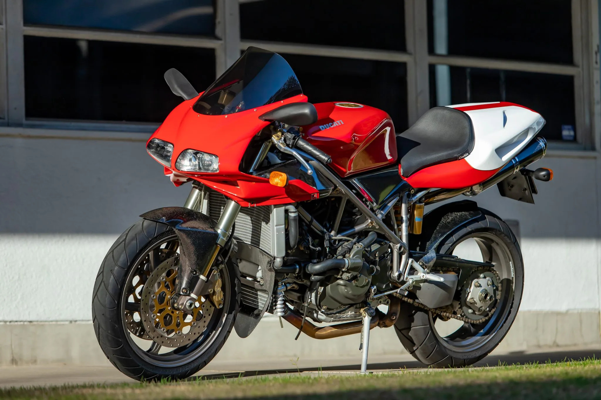A Ducati 996 motorcycle parked outdoors, showcasing its iconic design and vibrant red and white paint job