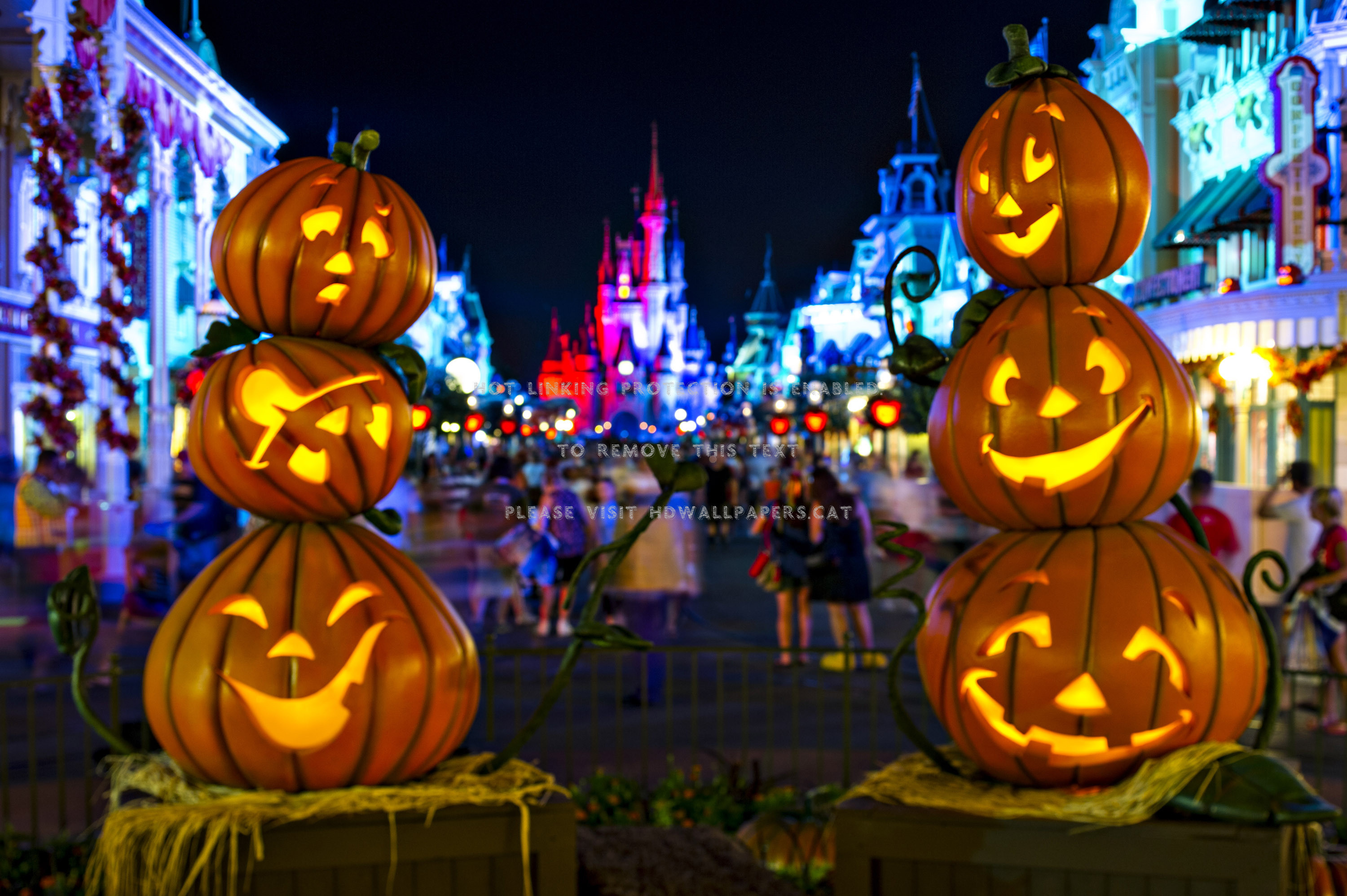 Three stacked carved pumpkins glow against the backdrop of a festively lit Disney castle during Halloween celebrations at a Disney theme park