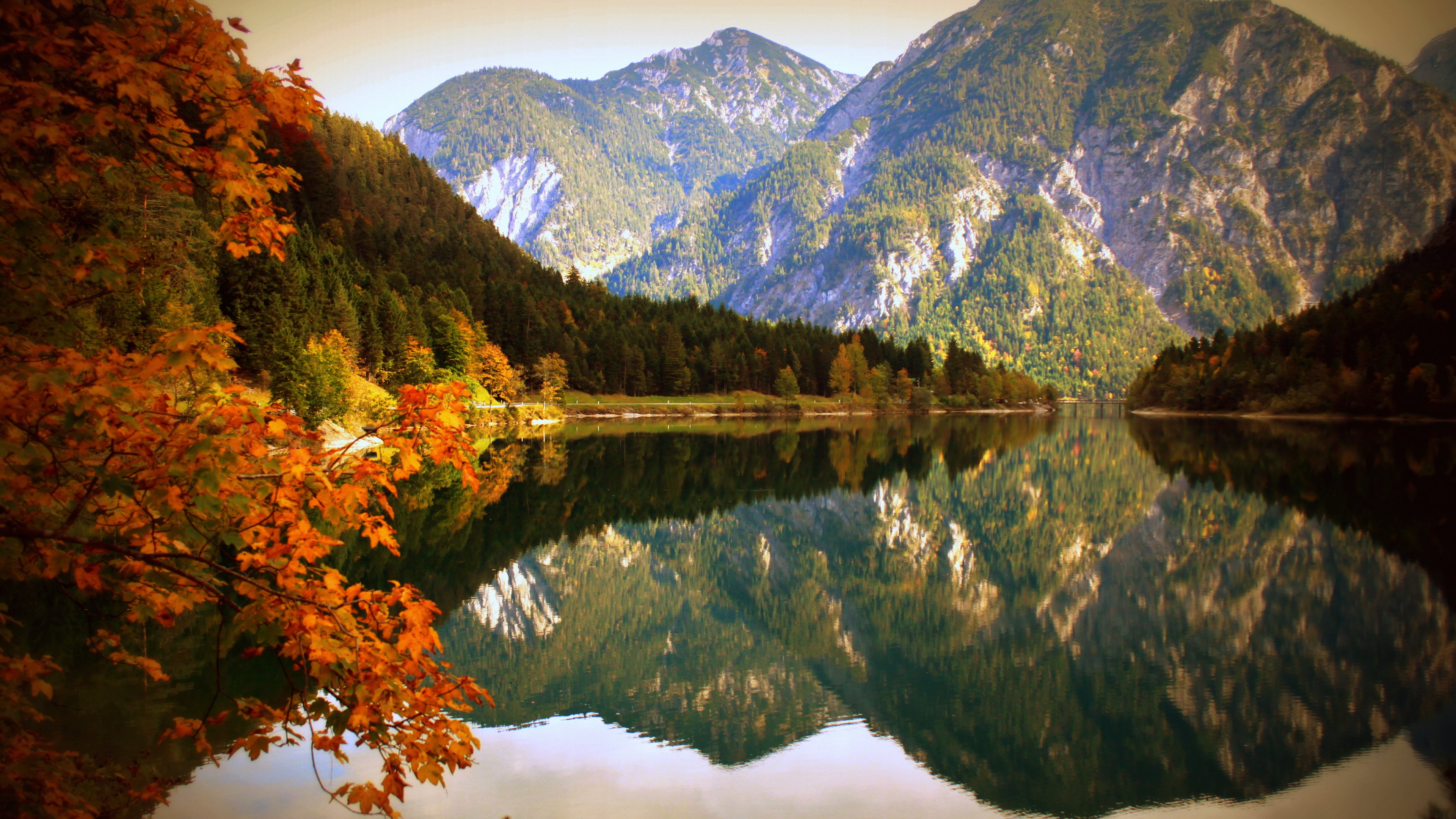 A stunning 4K wallpaper showcasing a crystal-clear lake reflecting the vibrant autumn colors of the surrounding mountain range