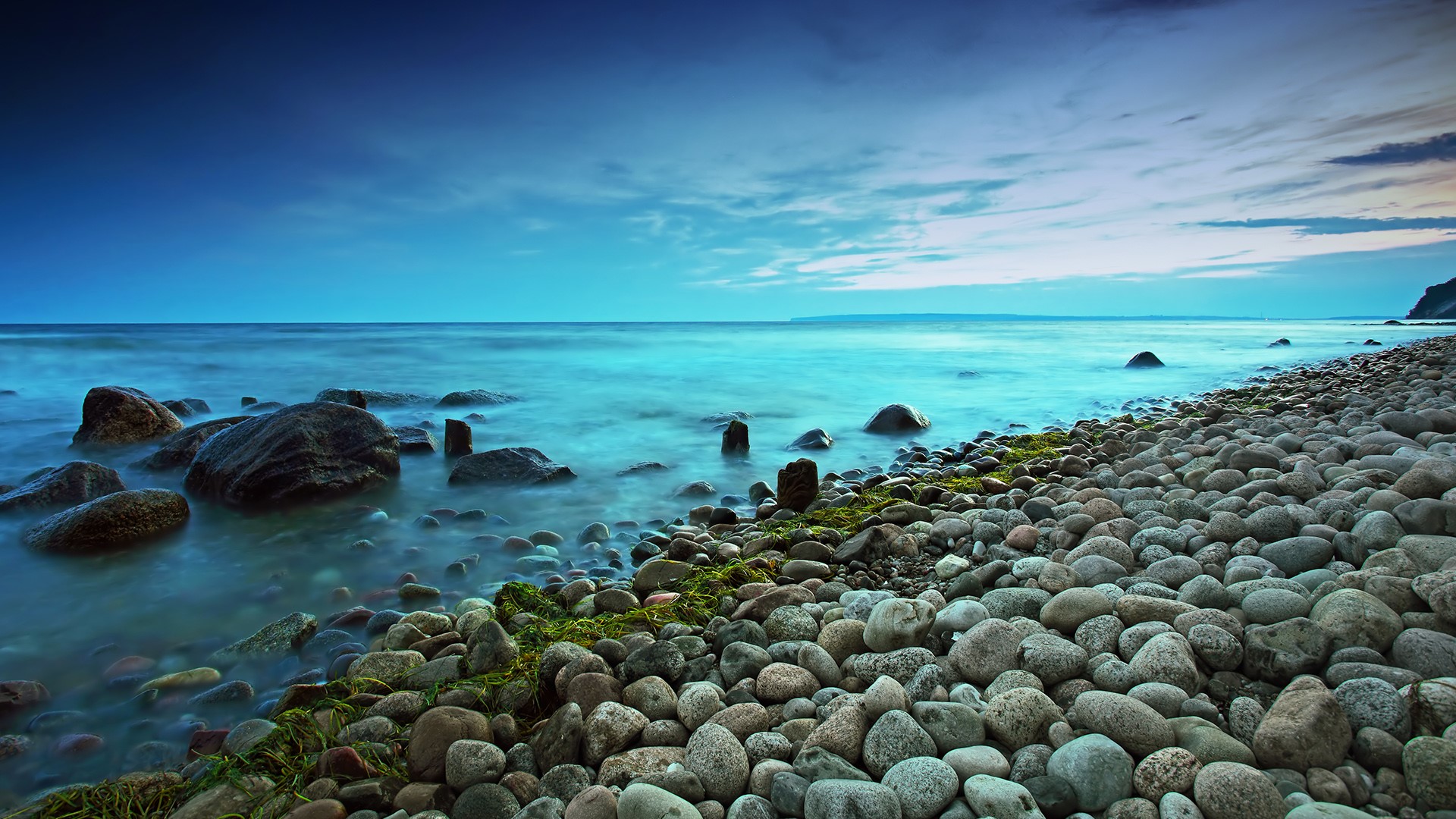 Serene rocky coastline at dusk with smooth water and blue sky