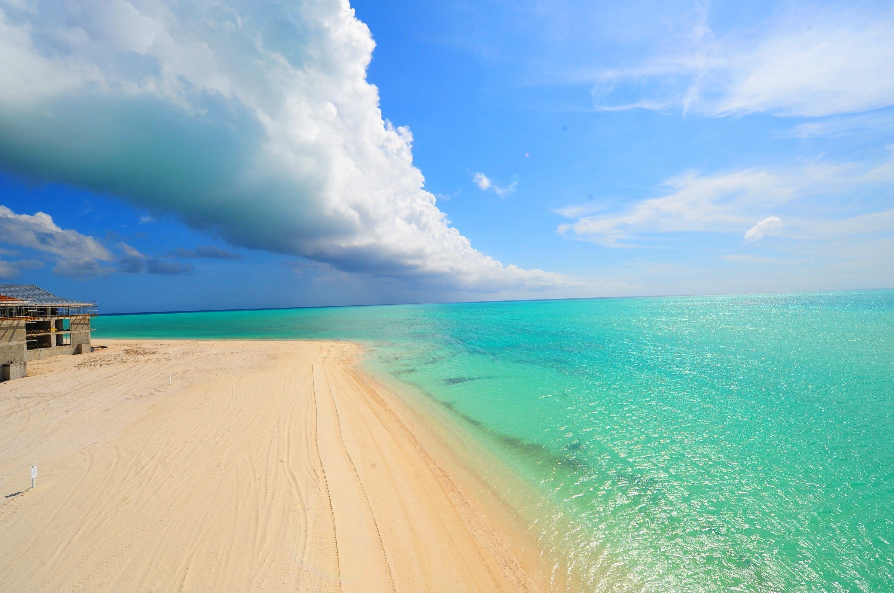 A breathtaking view of a pristine beach with turquoise water, white sand, and a dramatic cloudscape overhead