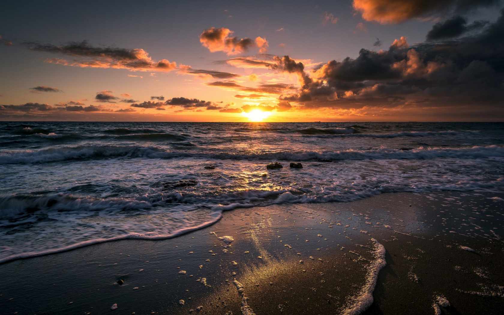 Sunset over a beautiful ocean with waves gently rolling onto the sandy beach
