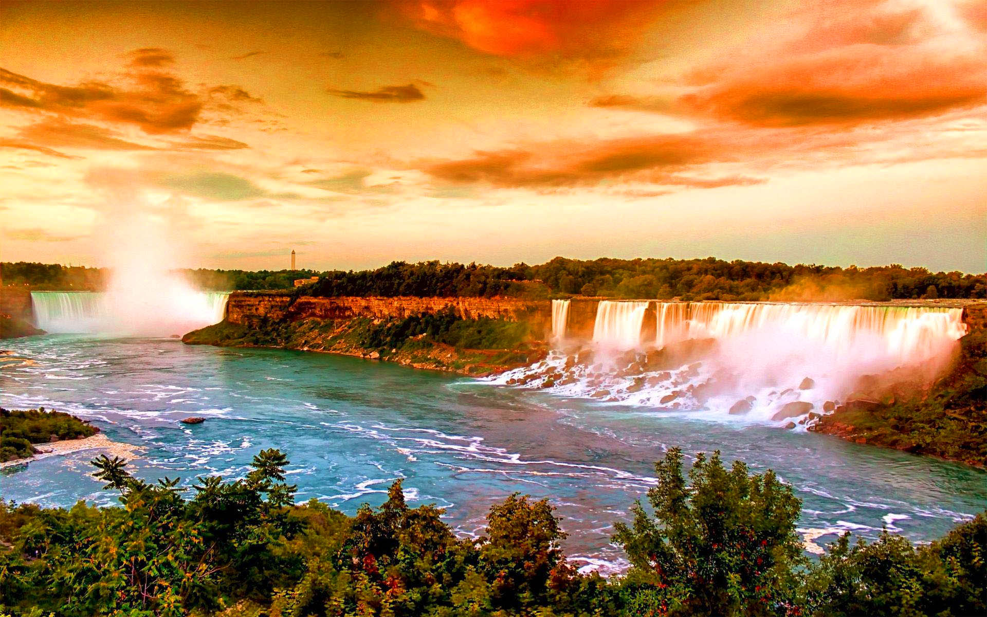 A breathtaking sunset over Niagara Falls, with vibrant orange and yellow hues illuminating the cascading water and lush green foliage