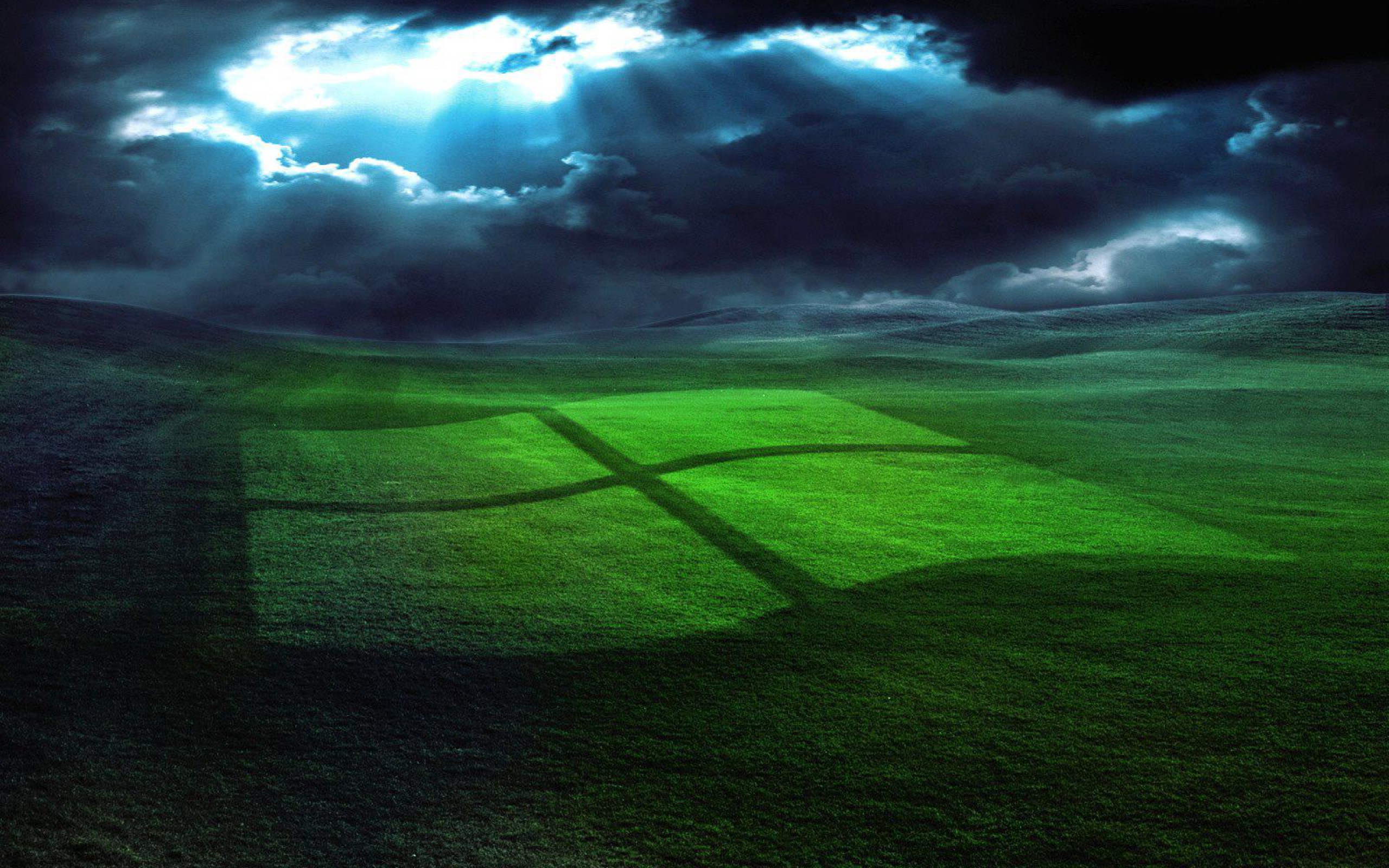A vibrant green Windows logo etched into a rolling grassy field under a dramatic, cloud-filled sky with beams of light breaking through
