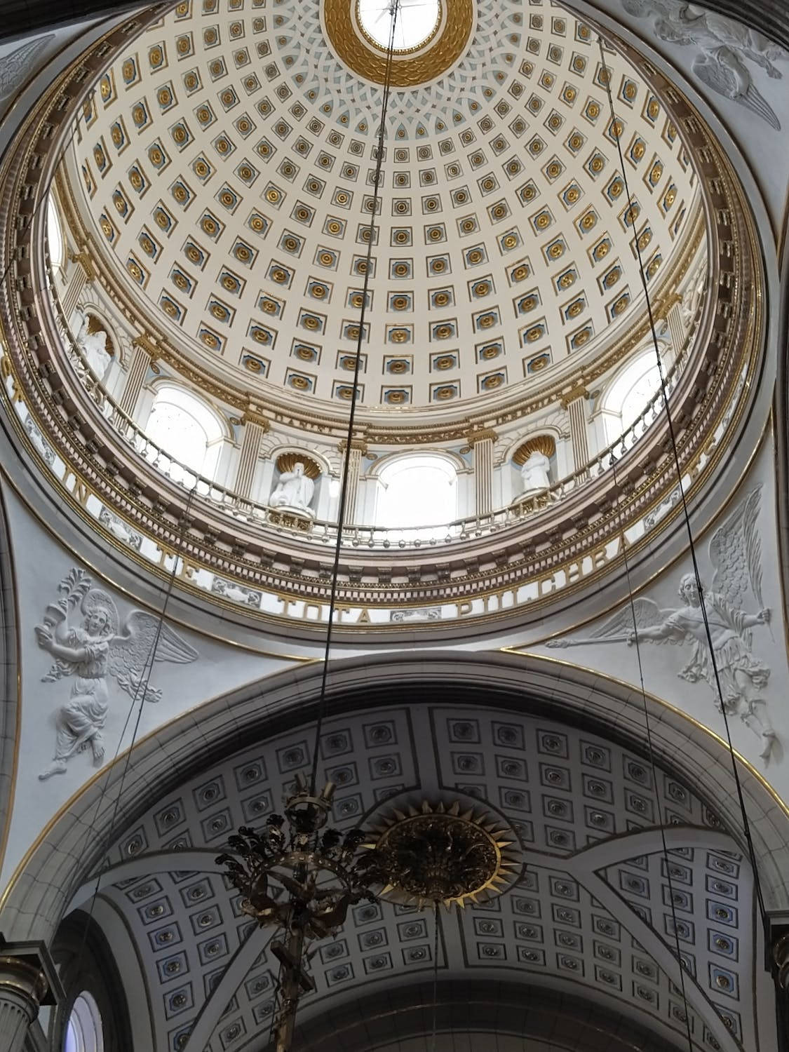 Low angle view of a church dome interior with intricate details, statues, and a chandelier
