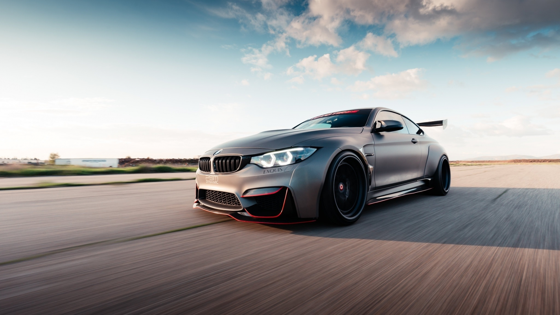 A tuned BMW M4 coupe speeding down a paved road