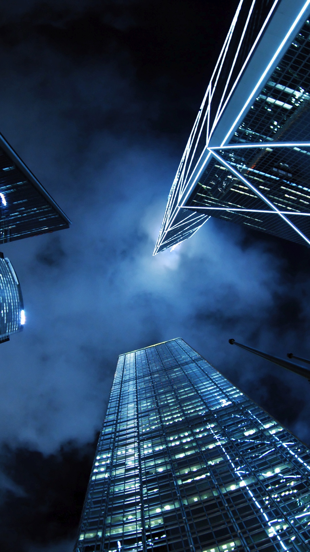 Low-angle shot of illuminated skyscrapers against a dark blue, cloudy night sky in a modern cityscape, ideal for a cool phone wallpaper