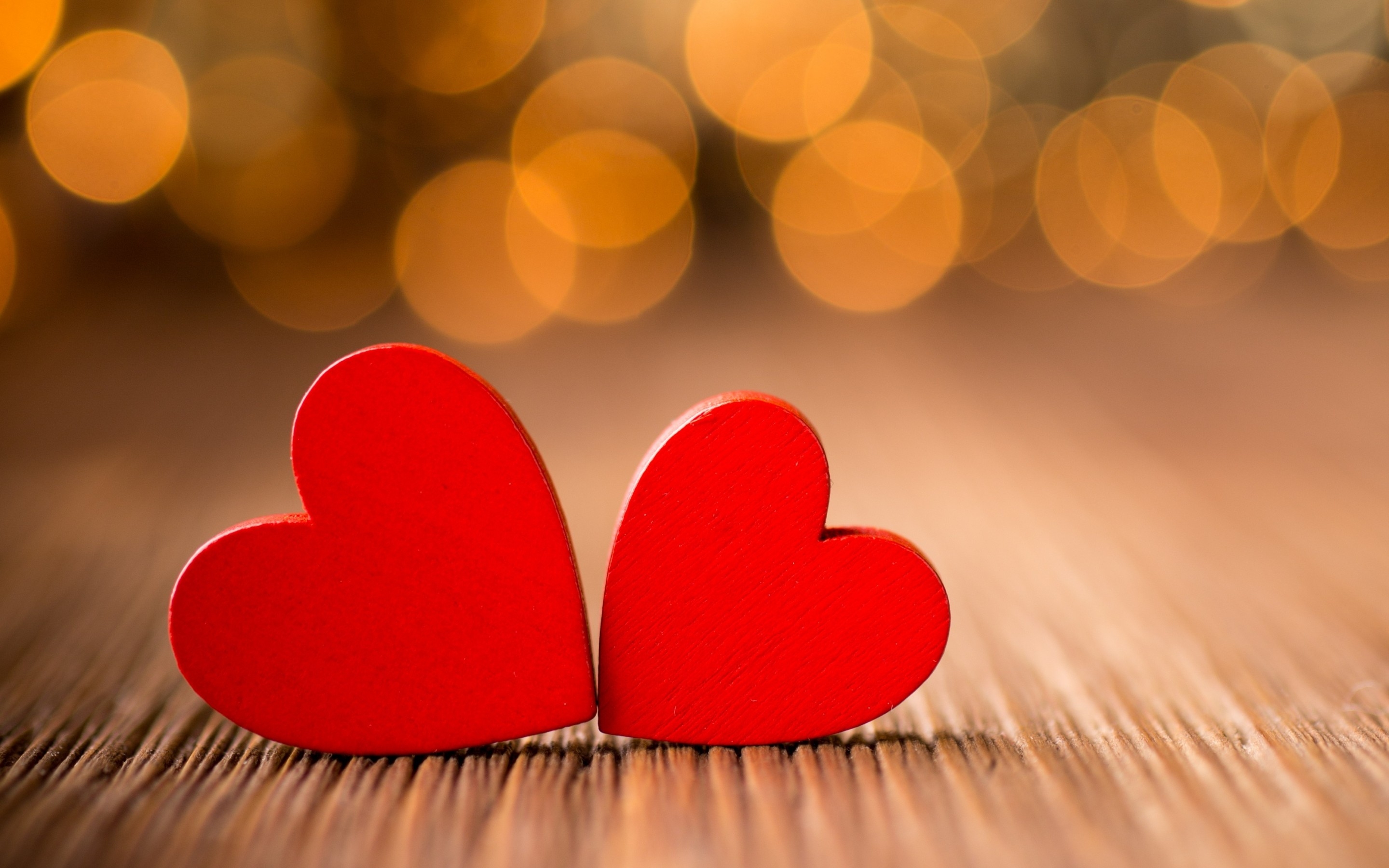Two red wooden hearts on a wooden surface with a warm, bokeh background, symbolizing love and affection