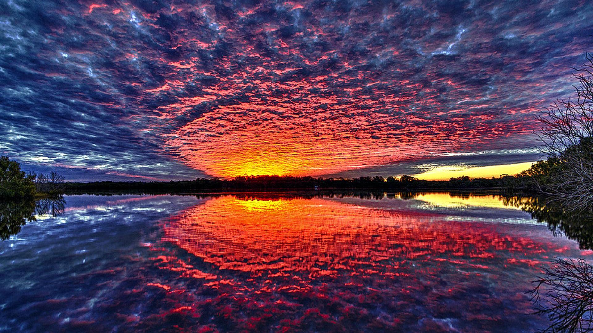 Vivid sunset reflected in a calm lake, creating a stunning mirror image of the colorful sky and clouds