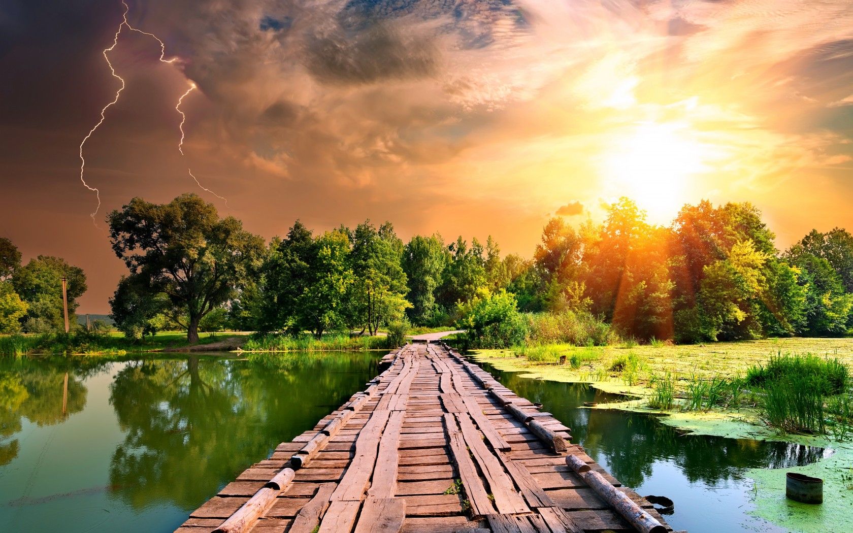 A breathtaking sunset illuminates a rustic wooden bridge stretching across a serene river, surrounded by lush greenery. Lightning adds a dramatic touch to the vibrant sky