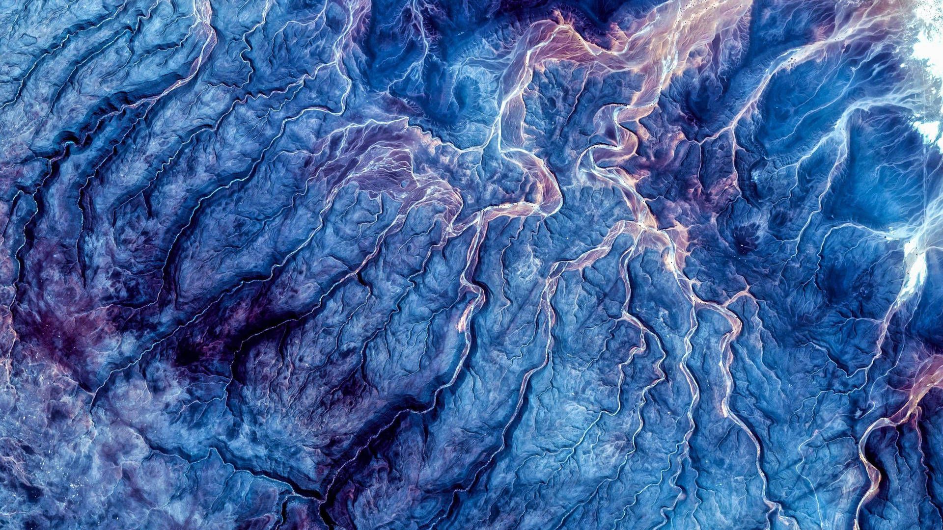 Abstract aerial view of a landscape with intricate patterns and textures in shades of blue and purple, resembling a network of veins or rivers