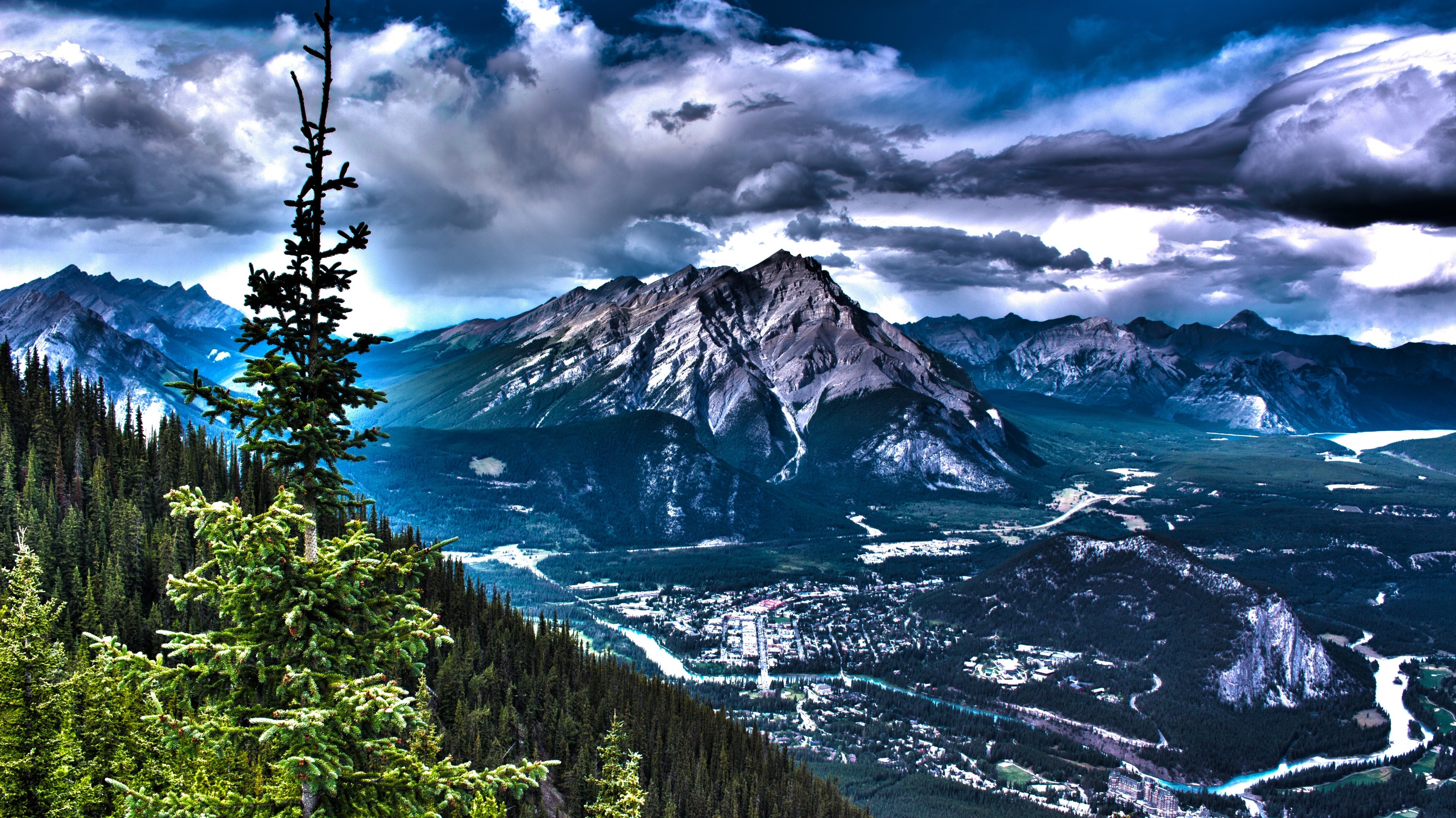 A breathtaking panoramic view of a mountain valley town nestled amidst towering peaks and lush evergreen forests under a dramatic sky