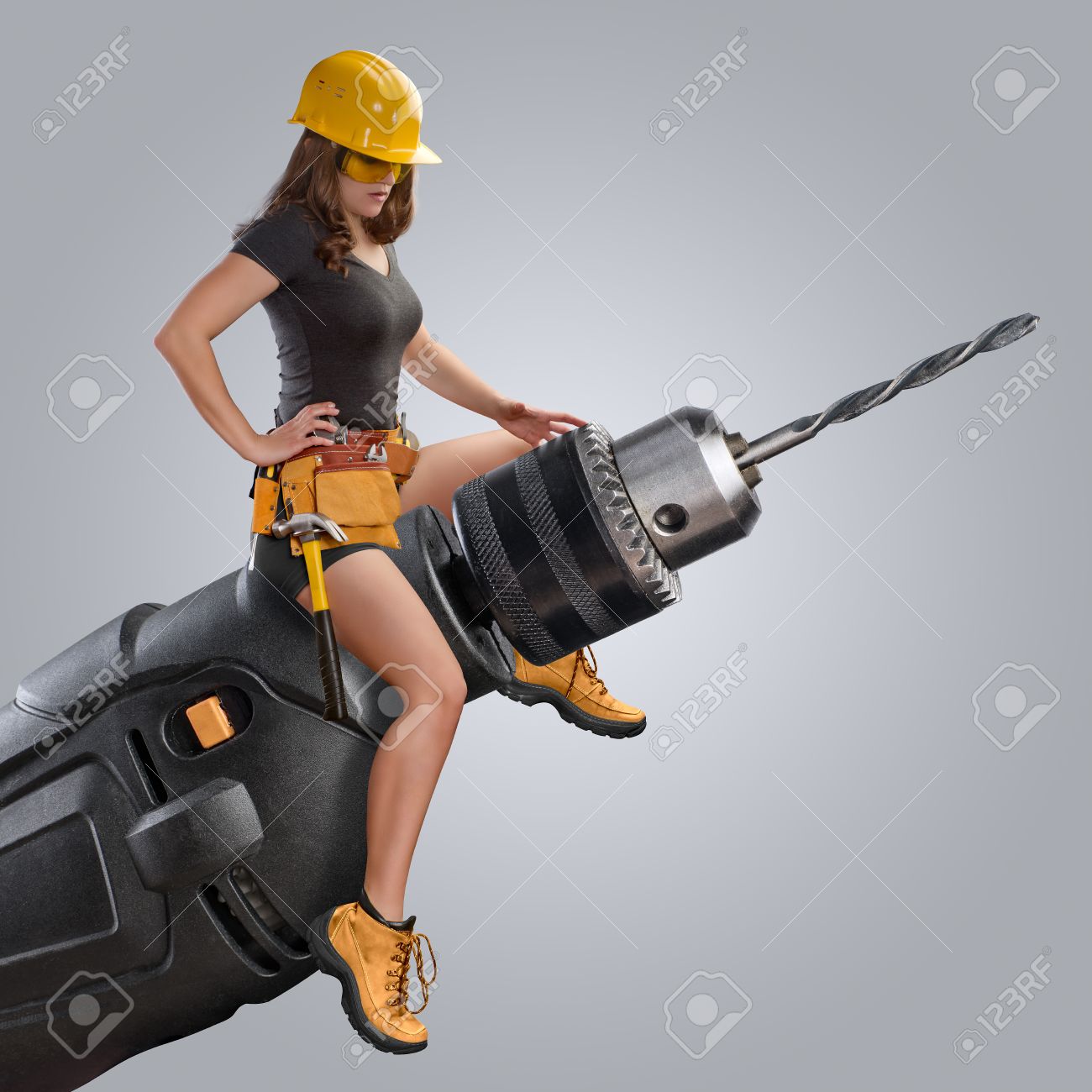 Worker Girl Sitting On A Drill Grey Background Stock Photo