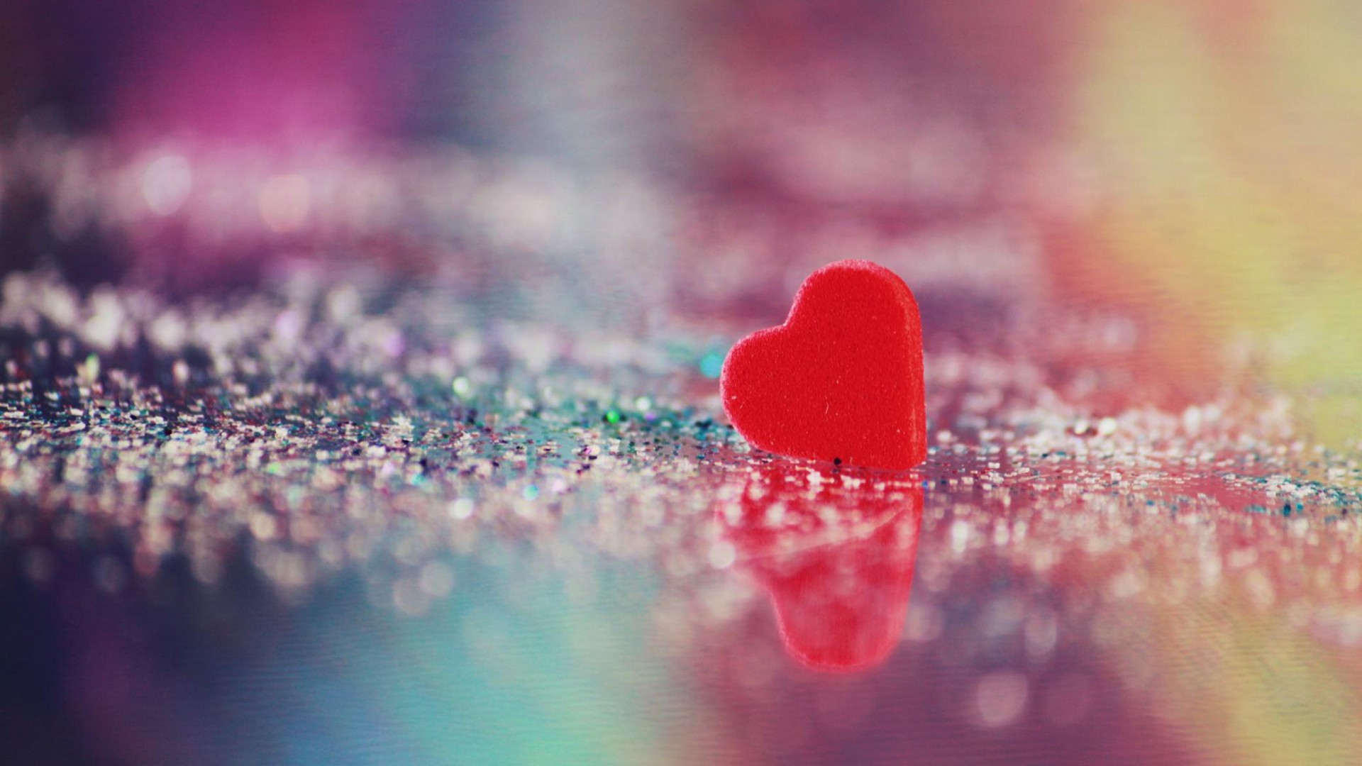 A small red heart on a glittery surface, reflecting in a soft, dreamy light. Perfect for Valentine's Day or any romantic occasion