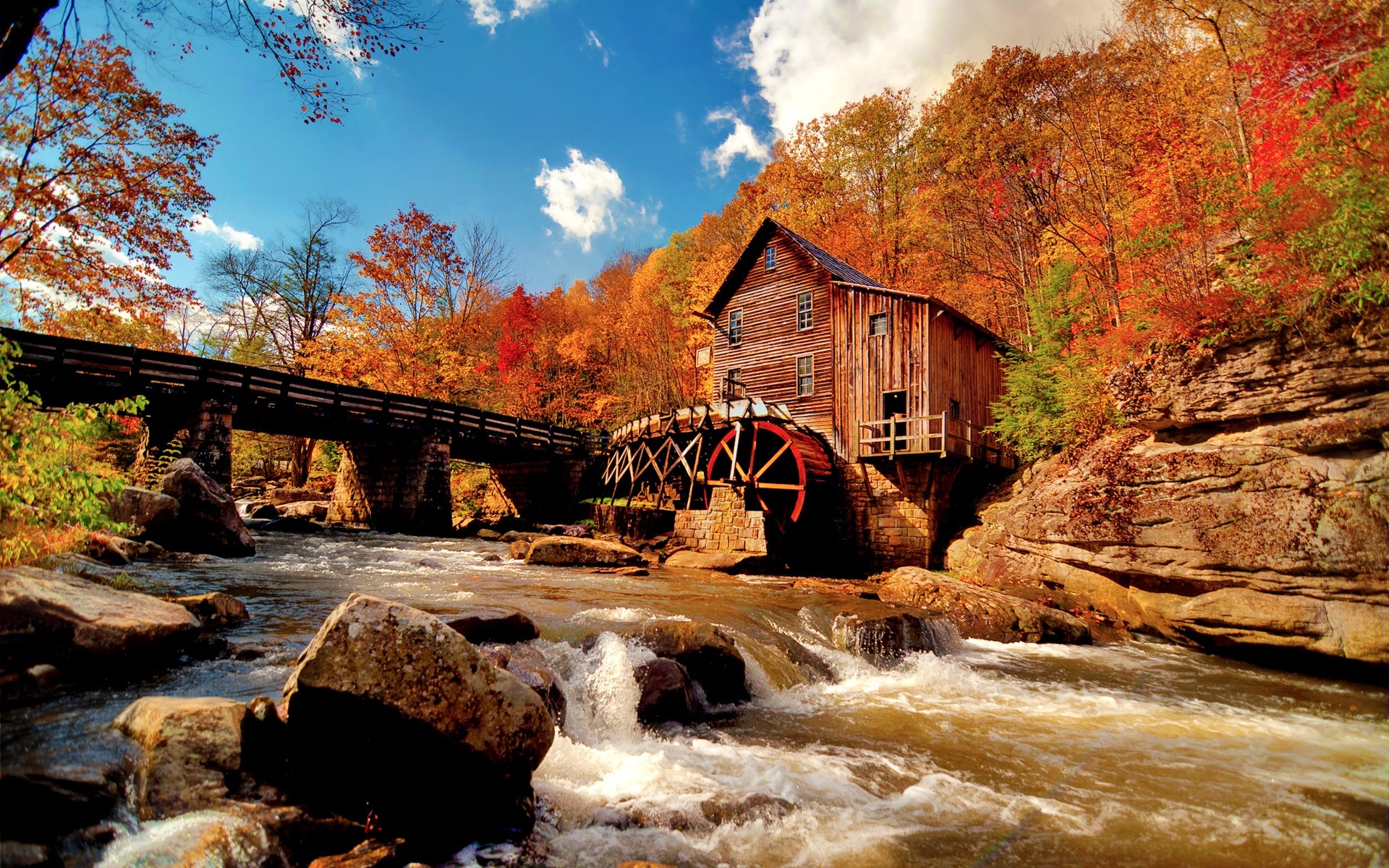 Scenic autumn landscape with an old grist mill, a wooden bridge, and a flowing river