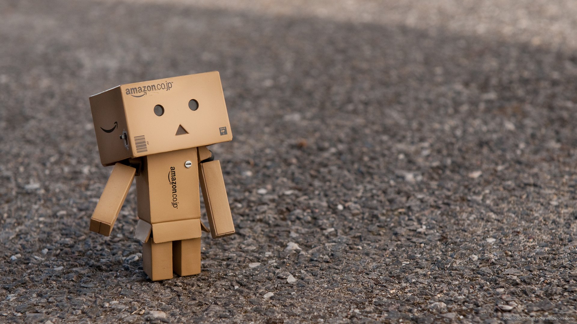 A small cardboard figure stands alone on a gravel road, conveying a sense of sadness and loneliness