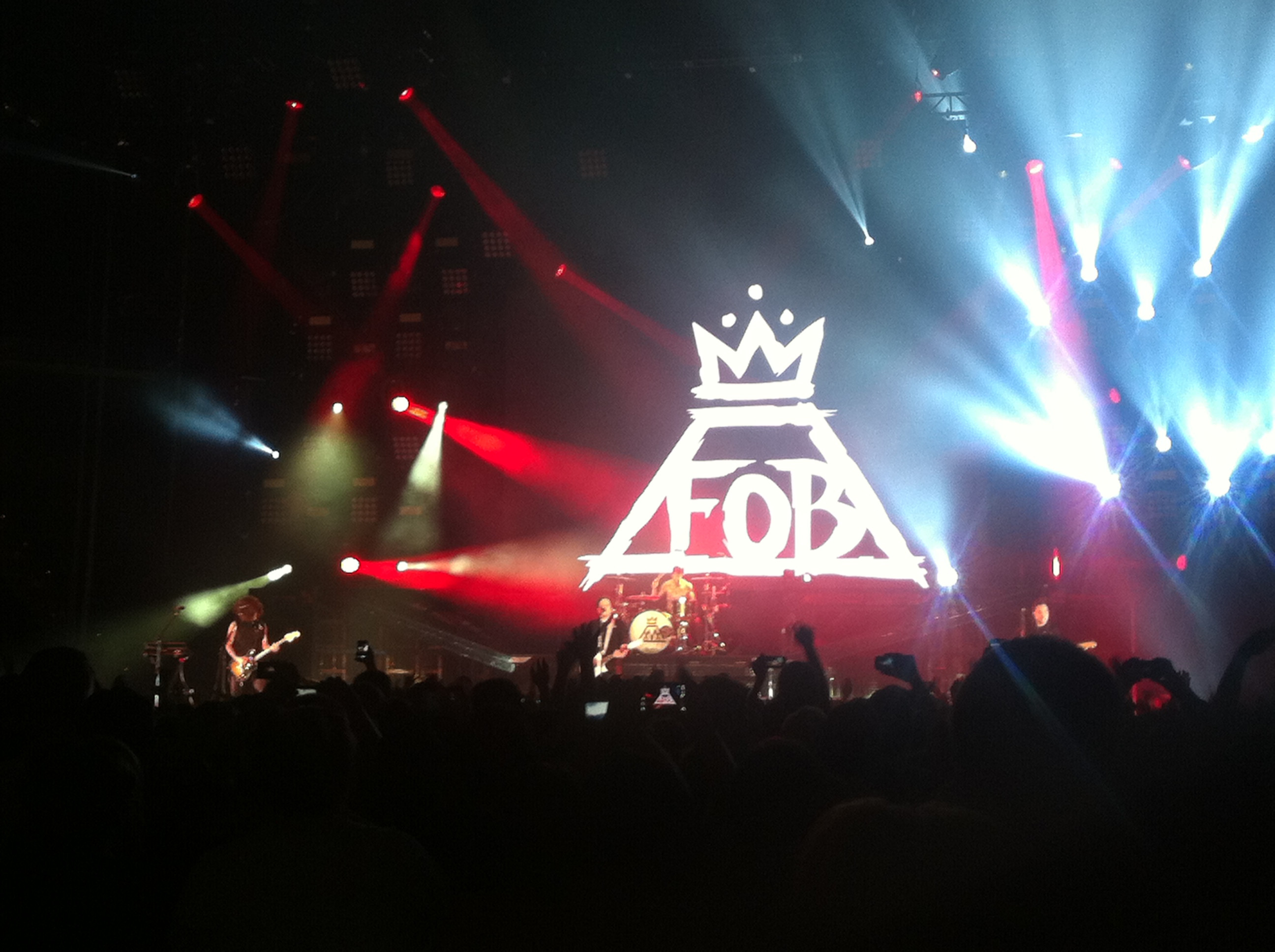 Fall Out Boy performing live on stage with their logo projected behind them
