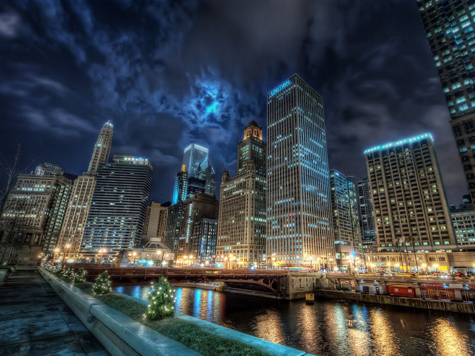 Stunning night view of the Chicago skyline with illuminated buildings and the Chicago River reflecting city lights. Christmas trees add a festive touch to the urban landscape