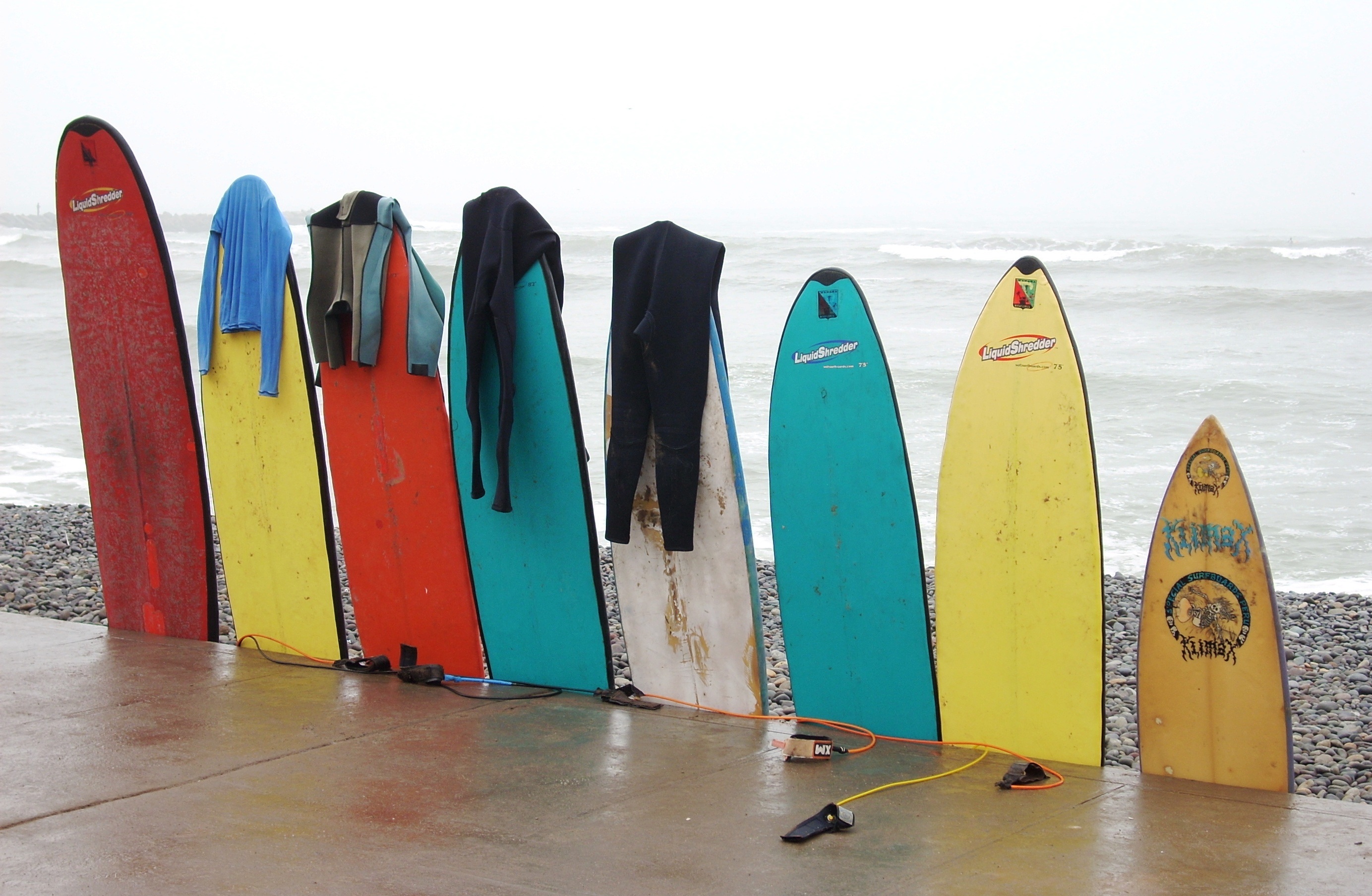 A Row Of Surfboards With Wetsuits Hanging Off Them HD Wallpaper