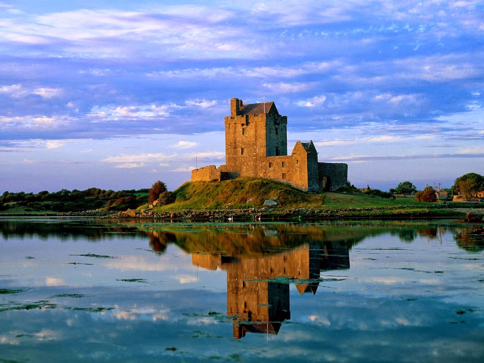 A majestic medieval castle stands on a small island in a tranquil lake, reflected perfectly in the still water under a beautiful sky